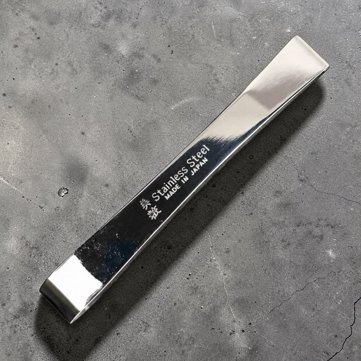 Small stainless steel fish bone tweezers on gray concrete