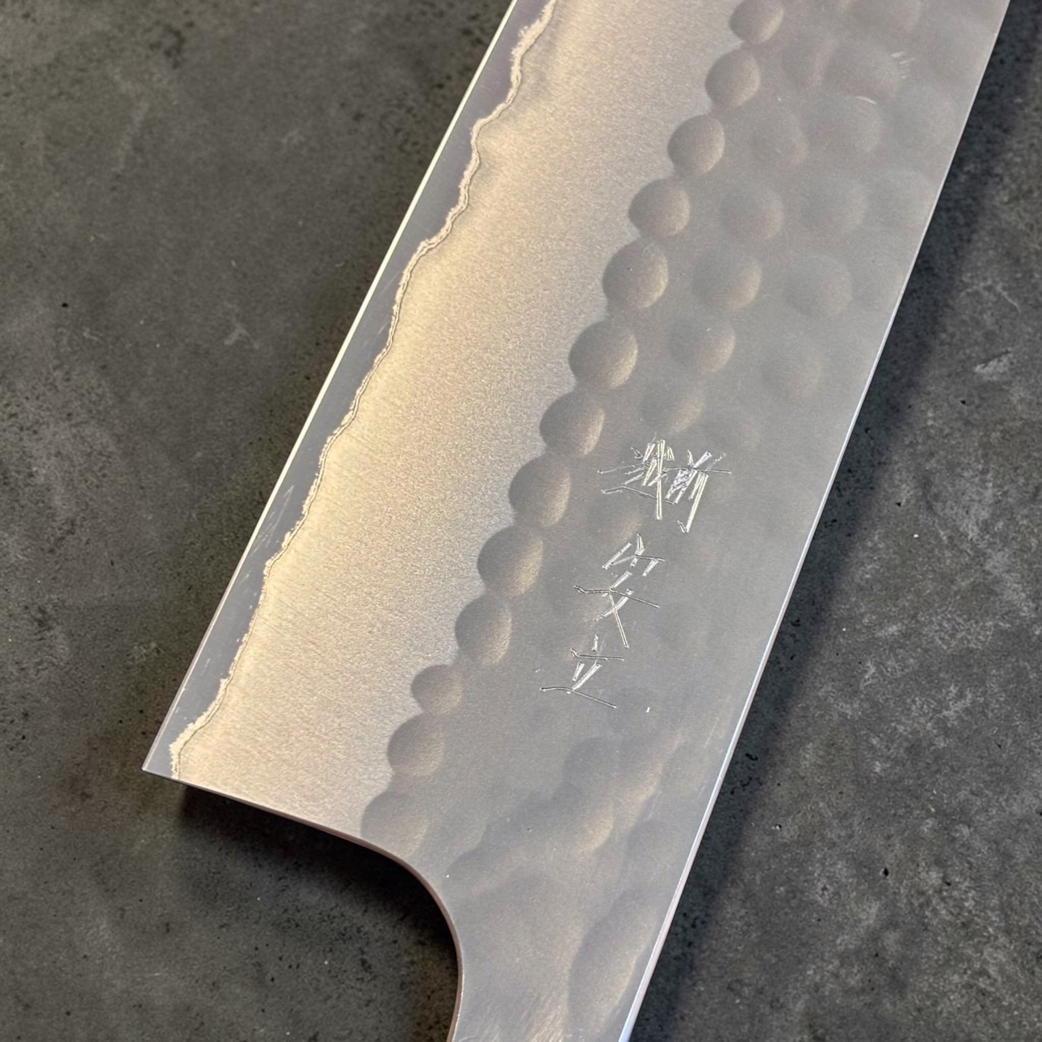 Close-up of Anryu kanji engraving, tsuchime hammering, and polished cladding line on Aogami #2 santoku