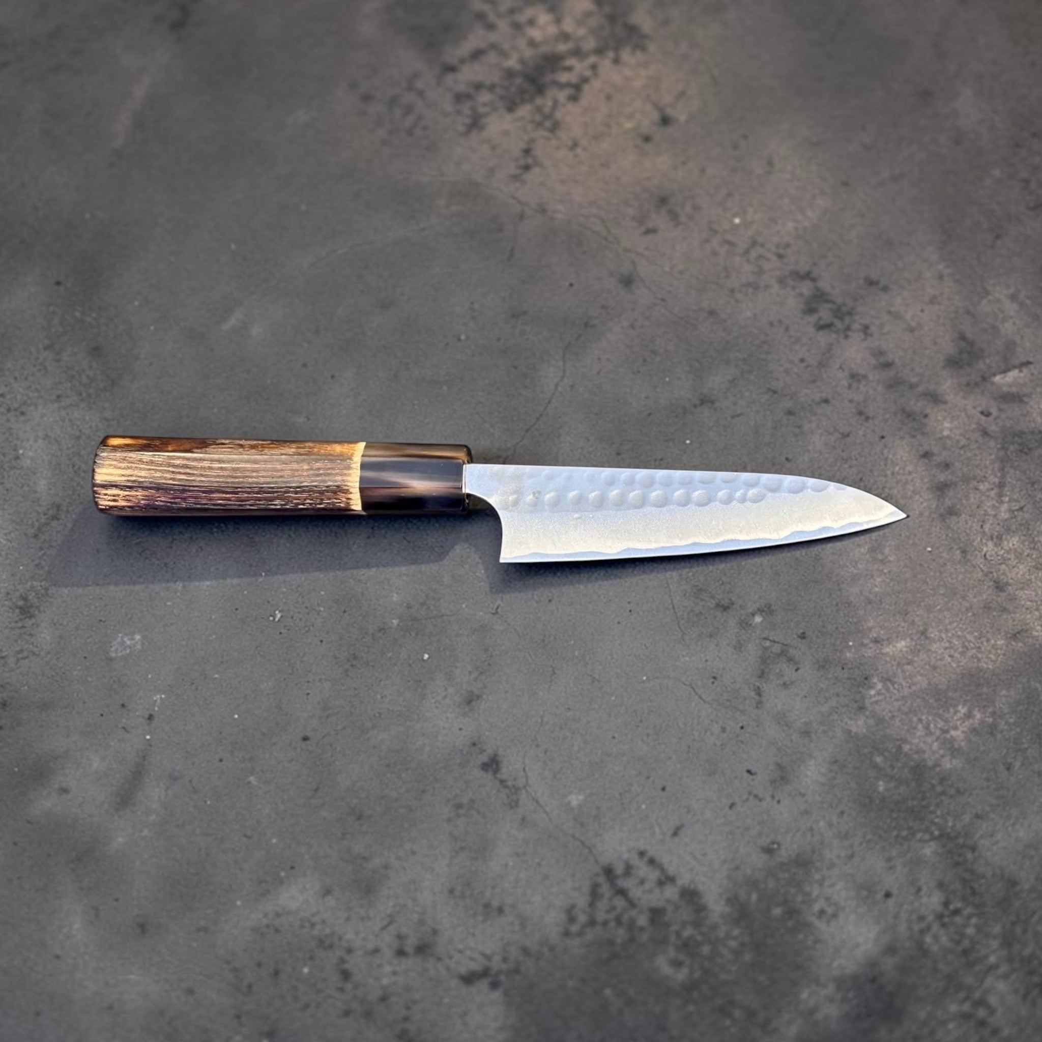 Anryu Aogami #2 Tsuchime Petty 120 mm with burnt wood handle and black buffalo horn ferrule, full profile view showing hammered tsuchime blade and wa handle.
