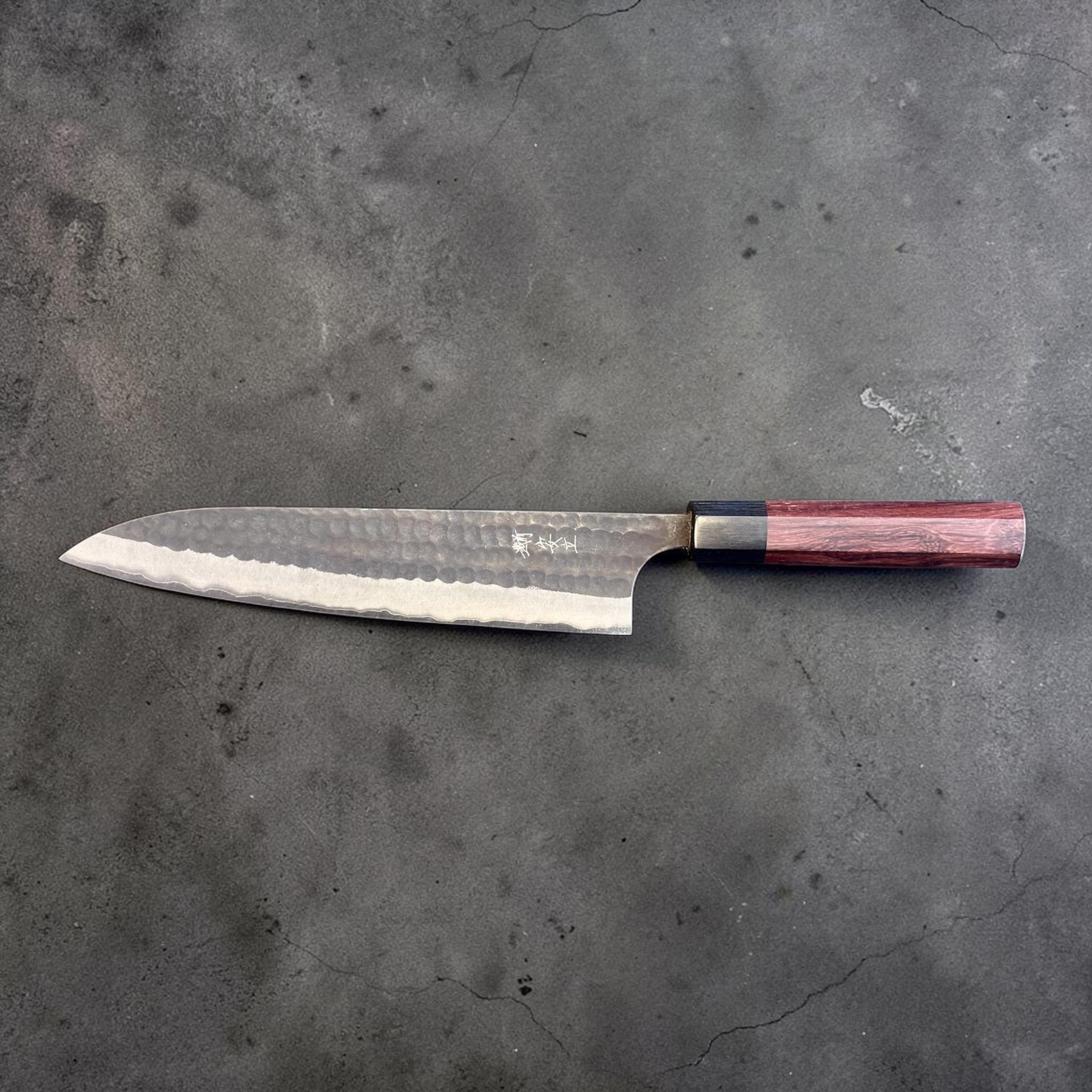 Anryu Aogami Super Kurouchi Gyuto 210 mm, angled close-up highlighting the hammered blade texture, polished bevel, kanji mark, and octagonal wa handle.