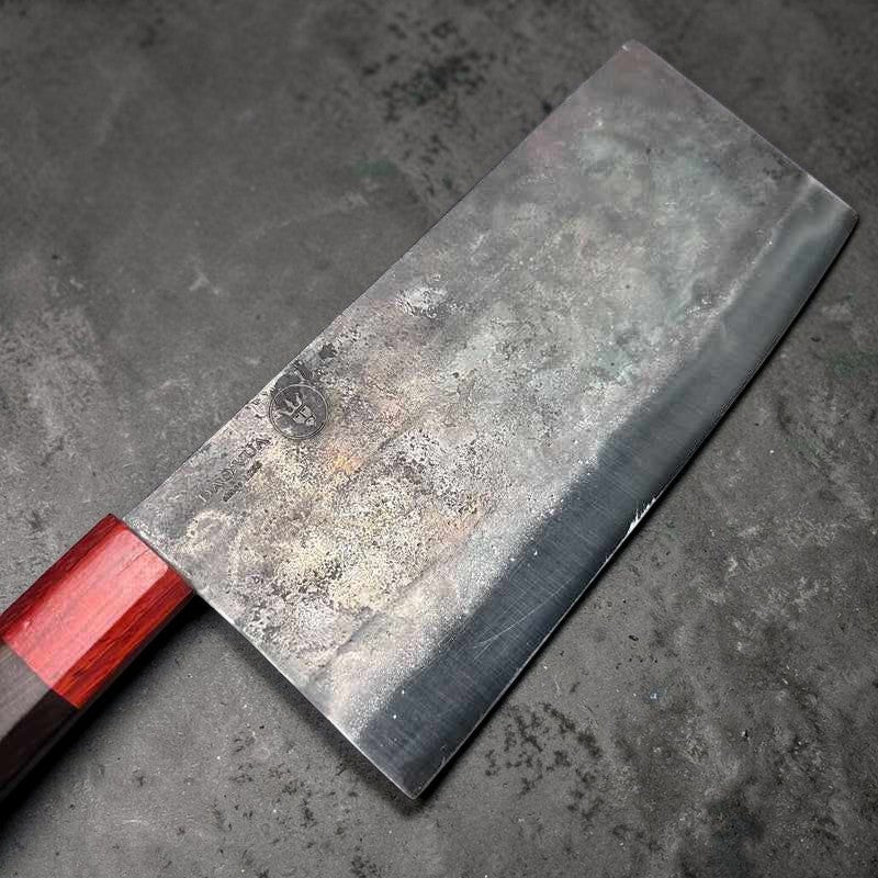 Angled view of the DAO VUA V3 52100 Chinese Cleaver showcasing the blade's edge and red handle on a light surface