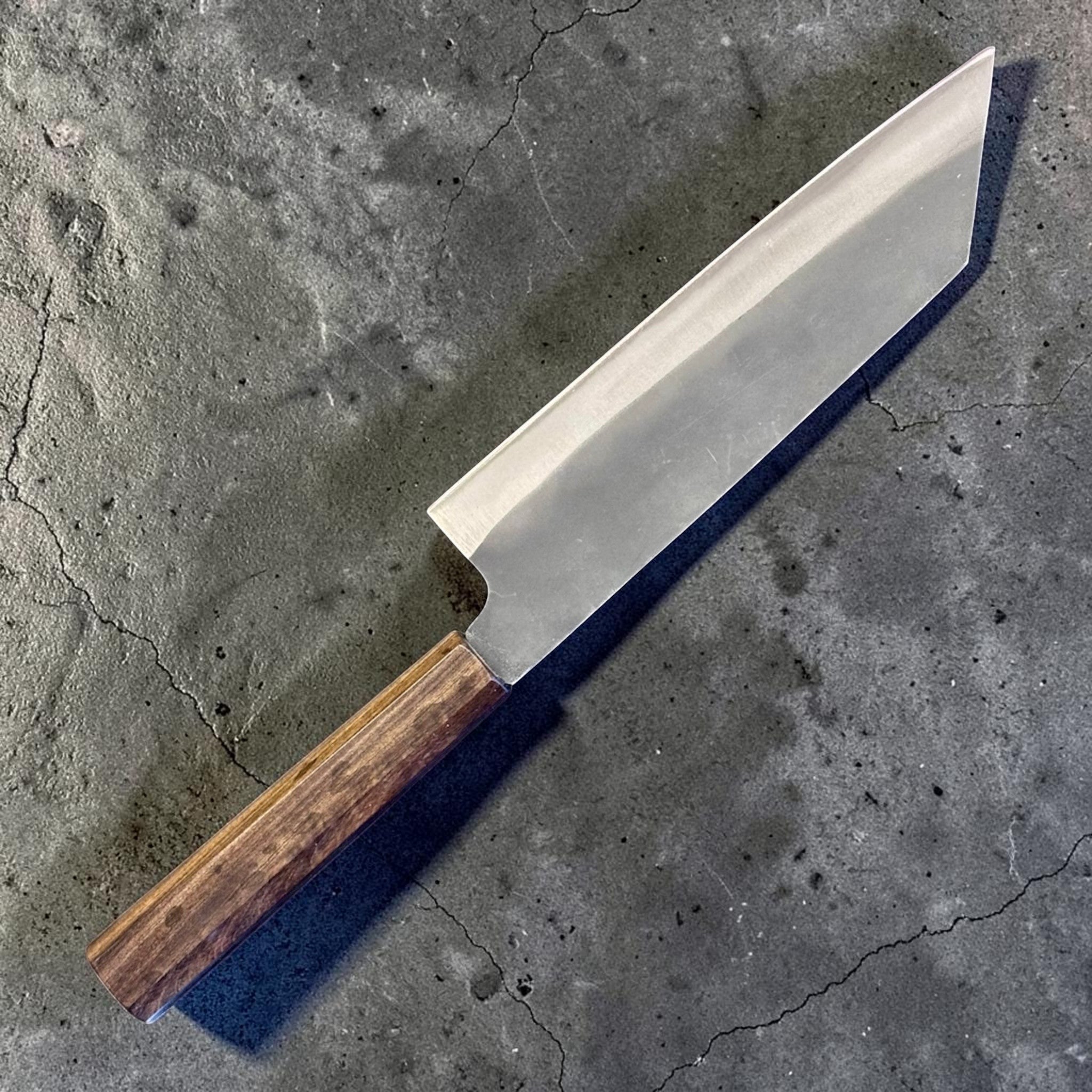 Hatsukokoro Blue #2 Kurouchi Bunka 190 mm with mono ebony handle, angled back-side product photo highlighting the rustic kurouchi blade road, tall heel, and faceted octagonal ebony wa handle.