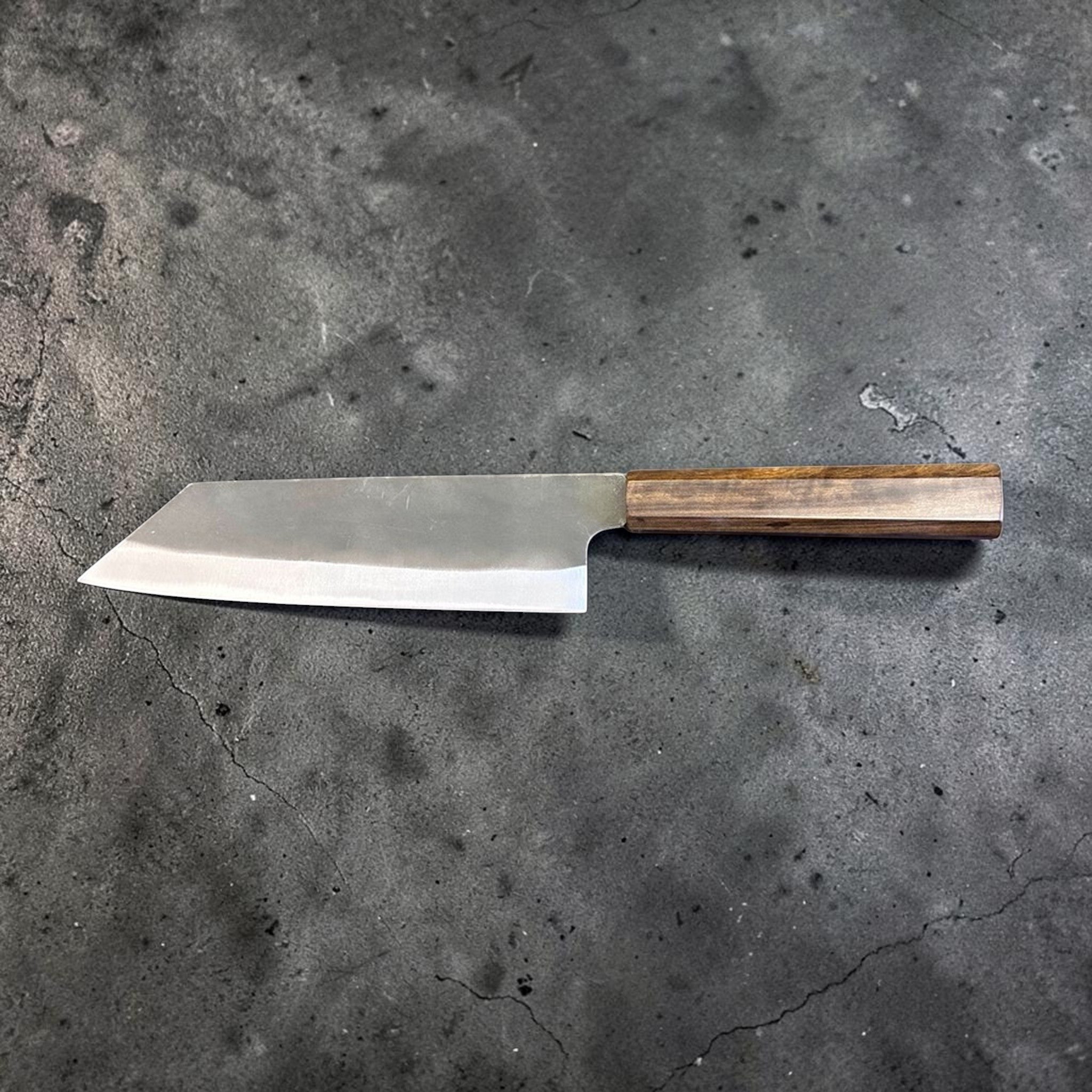 Hatsukokoro Blue #2 Kurouchi Bunka 190 mm with mono ebony handle, full profile back-side view showing the blade geometry, kurouchi finish, and clean contrast between the dark upper blade and polished cutting edge.