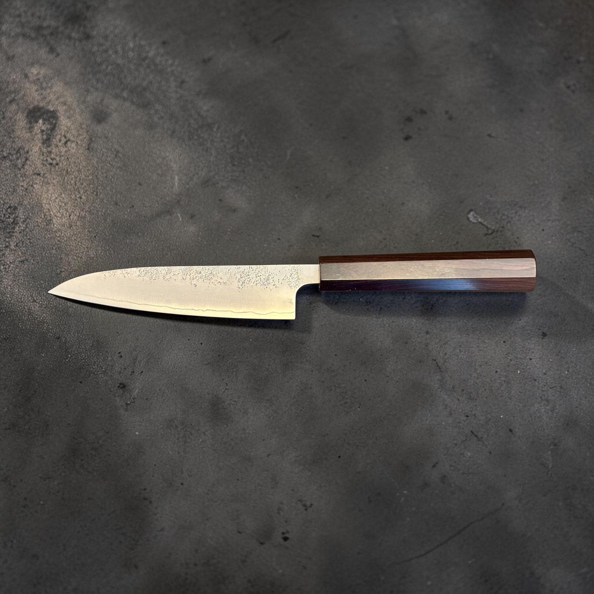 Hatsukokoro Ginrei Silver #3 Petty 130 mm with mono ebony handle, full profile view on dark textured background.