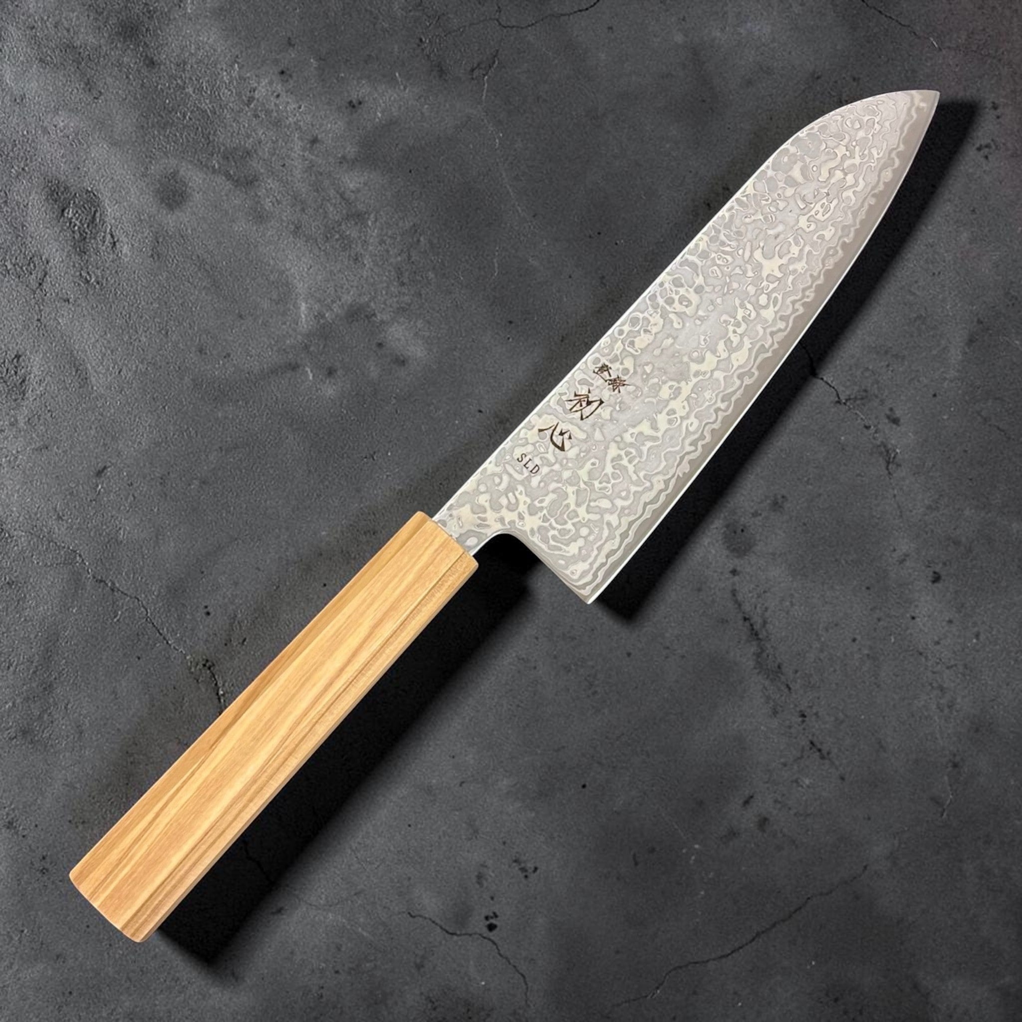 Hatsukokoro Hikari SLD Damascus Santoku 170 mm with olive wood handle, angled hero shot; close-up of damascus pattern on the blade.