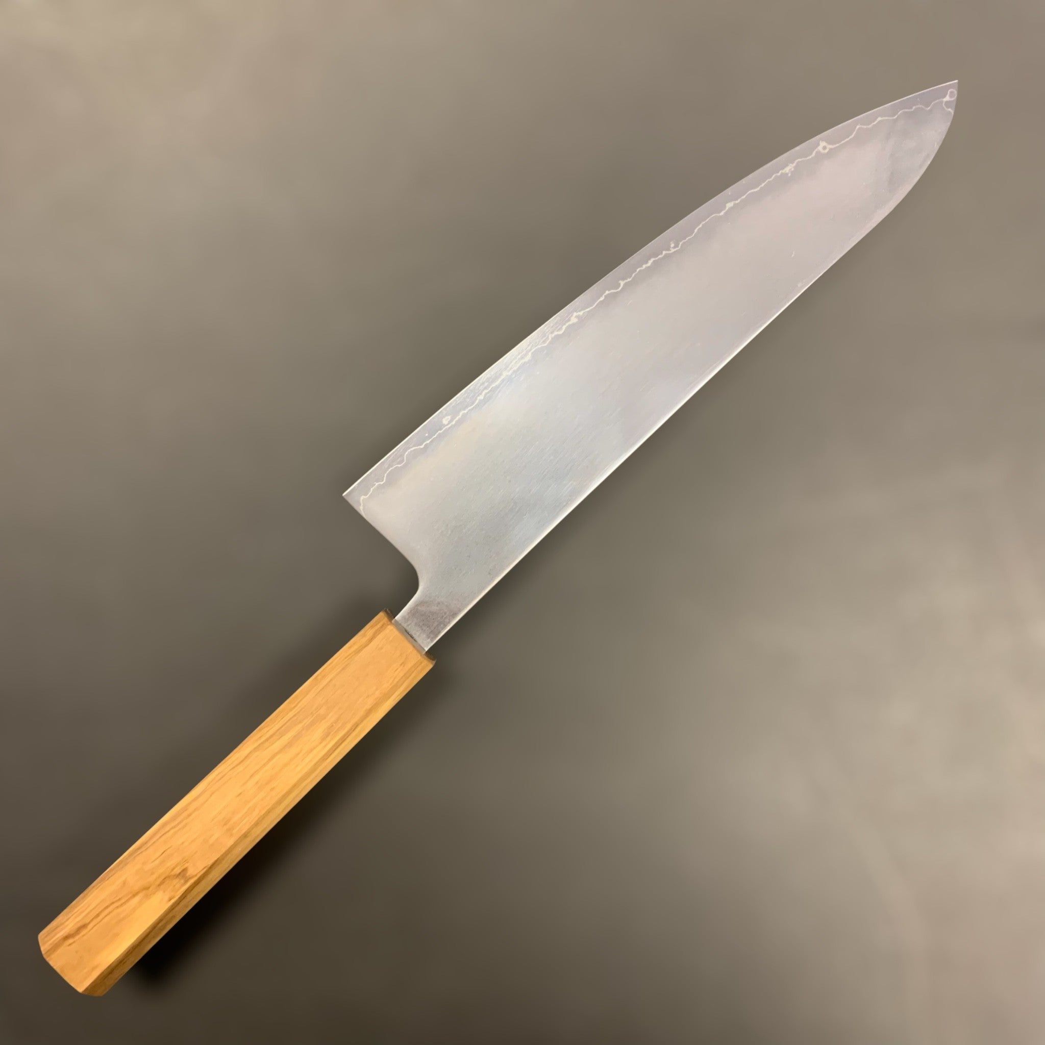 Hatsukokoro Hikari SLD Migaki Gyuto 210 mm, full left-side profile on dark background highlighting the hamon line and migaki finish.