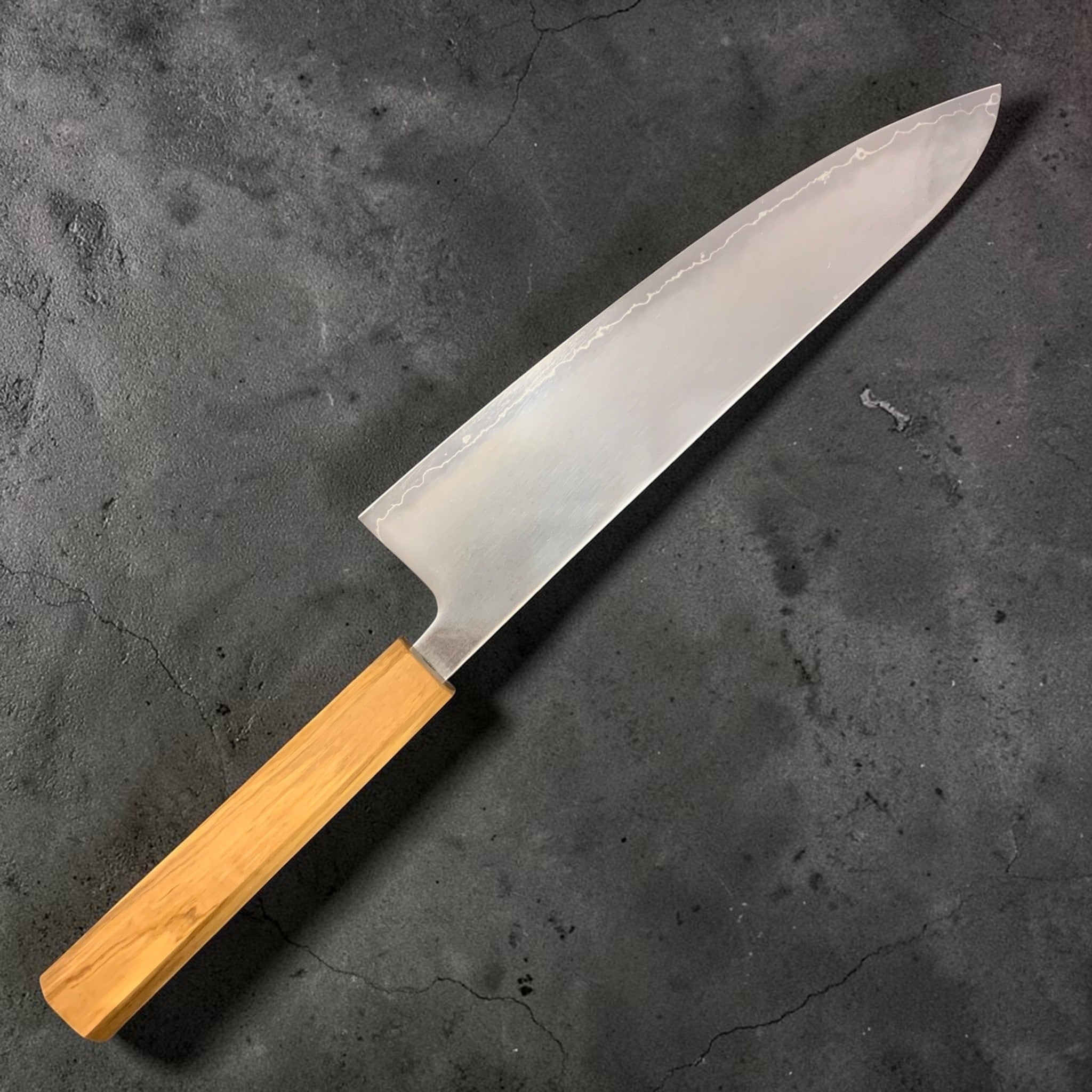 Hatsukokoro Hikari SLD Migaki Gyuto 210 mm, full left-side profile on dark background highlighting the hamon line and migaki finish.