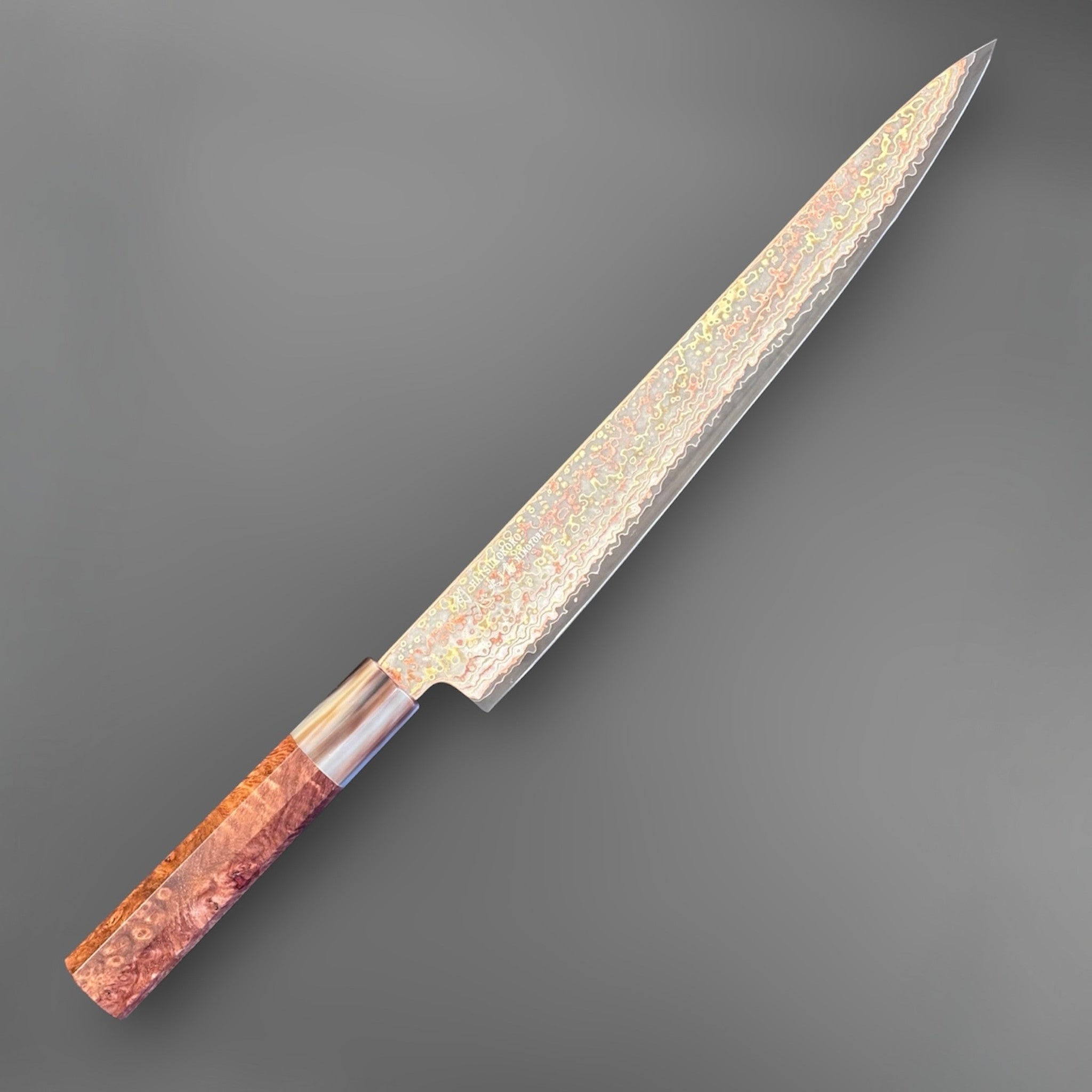 Hatsukokoro Hinotori V-Toku2 Rainbow Damascus Sujihiki 270 mm, reverse angled product view showing long slicing blade and layered finish.