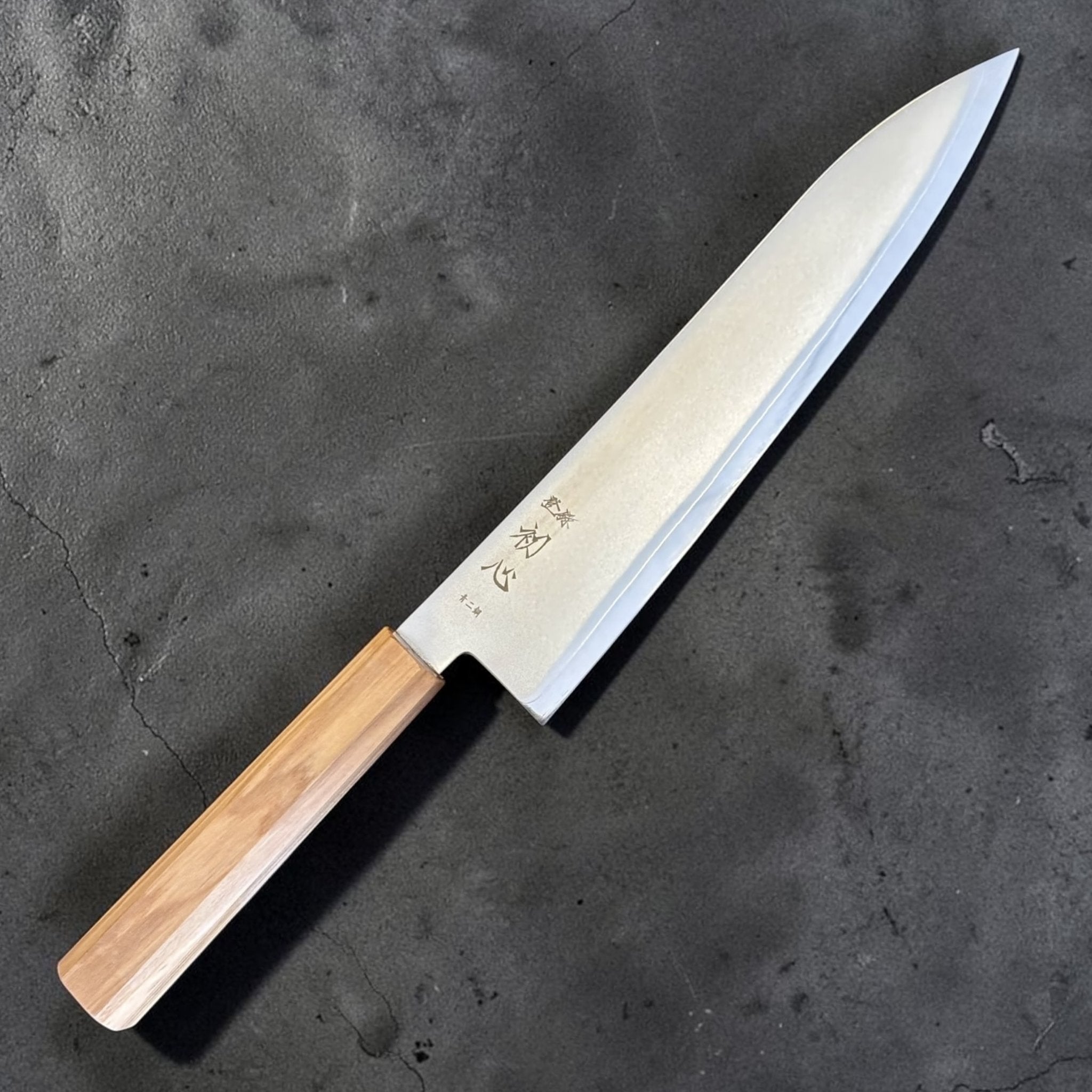 Hatsukokoro Kaijin Blue #2 Gyuto 210 mm with mono olive wood handle, angled full-knife product view on dark textured background.