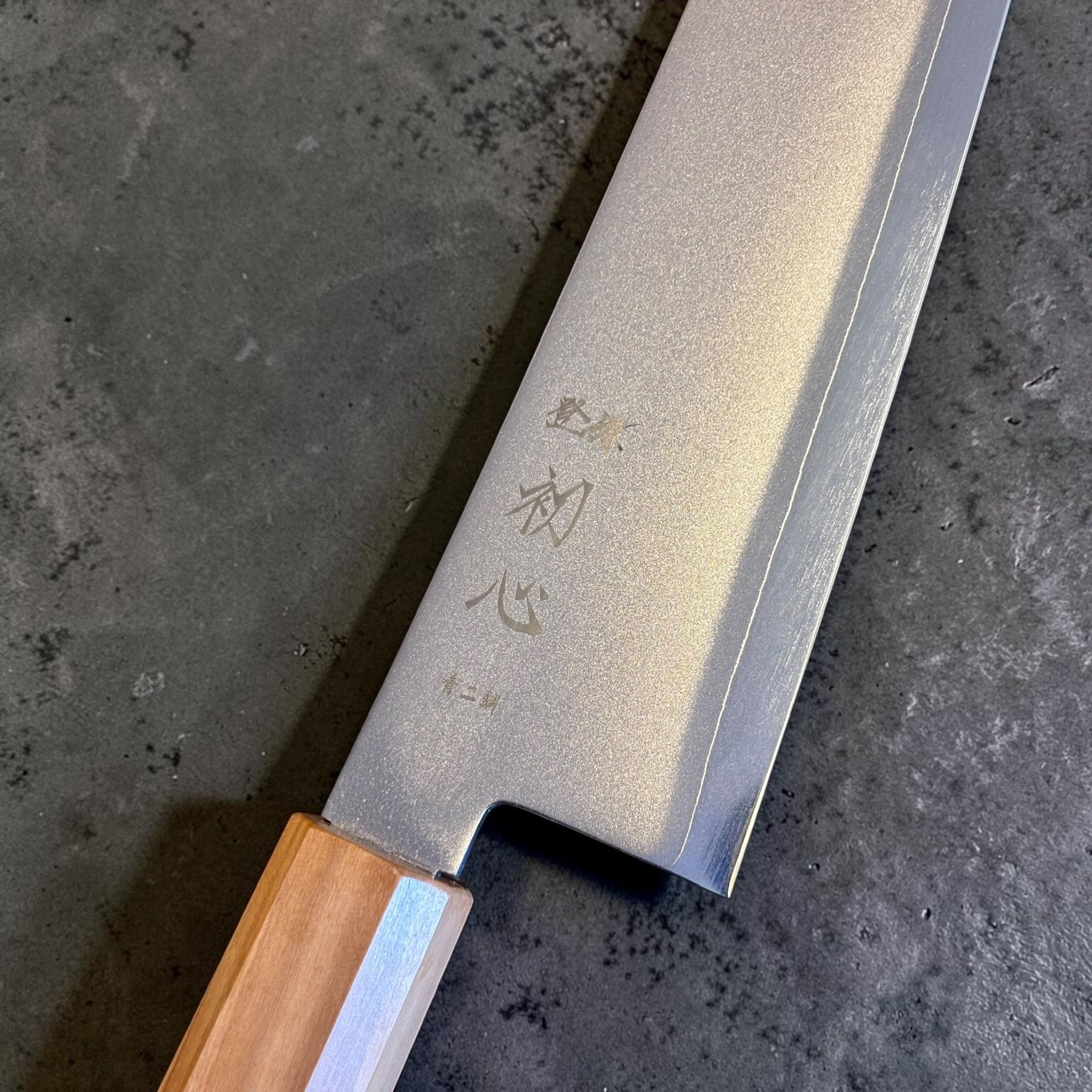 Close-up of the Hatsukokoro Kaijin Kiritsuke Gyuto blade kanji, migaki finish, and stainless cladding.