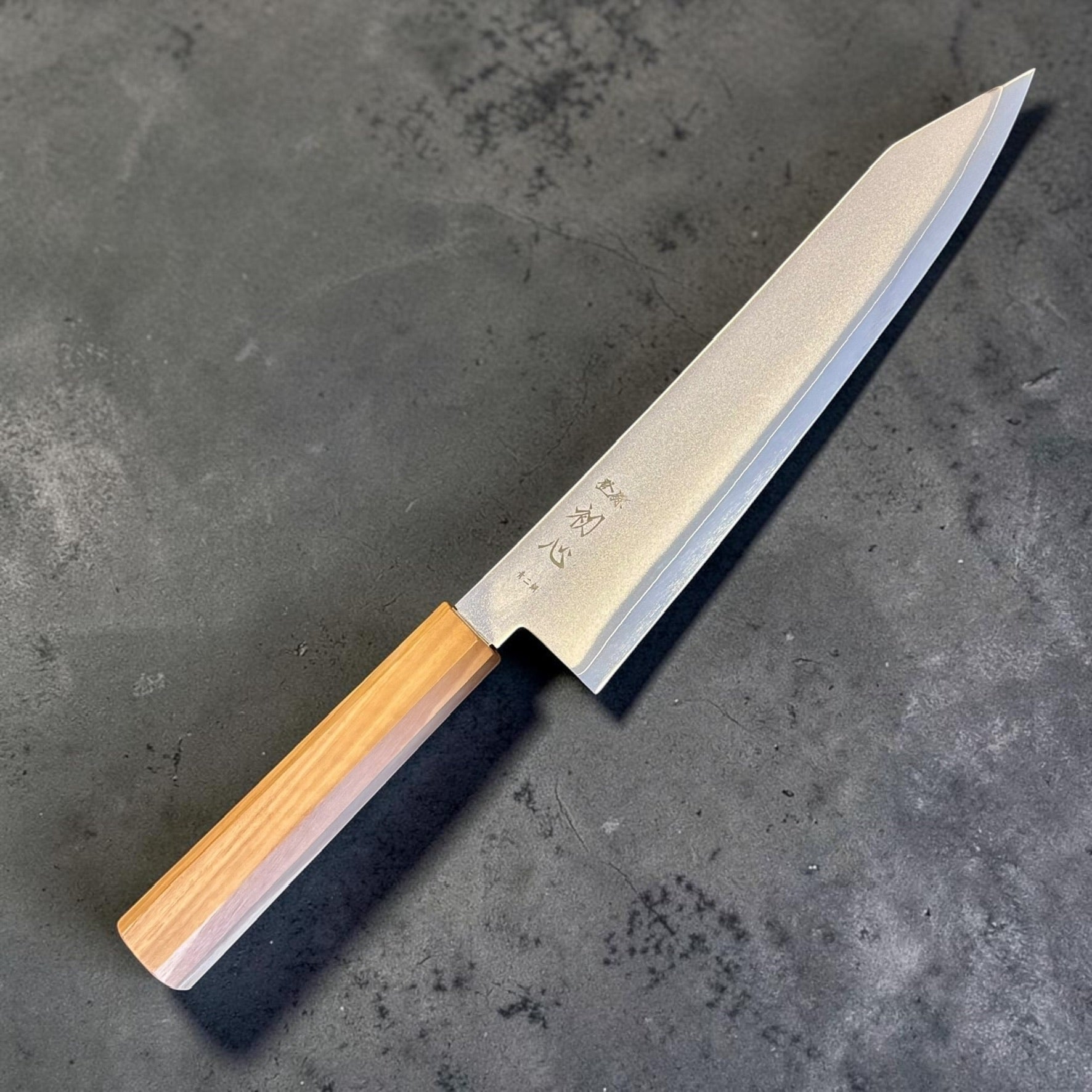 Hatsukokoro Kaijin Blue #2 Kiritsuke Gyuto 210mm with mono olivewood handle, angled view showing blade kanji and K-tip.