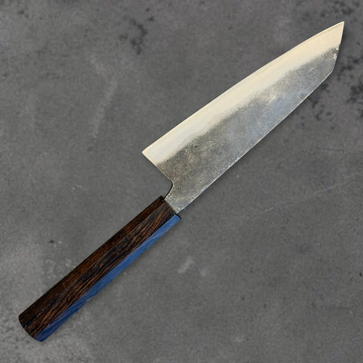 Angled reverse view of the Hatsukokoro Kurogane Blue #2 Kurouchi 140mm bunka with ebony handle, showing the blade shape, finish, and handle.