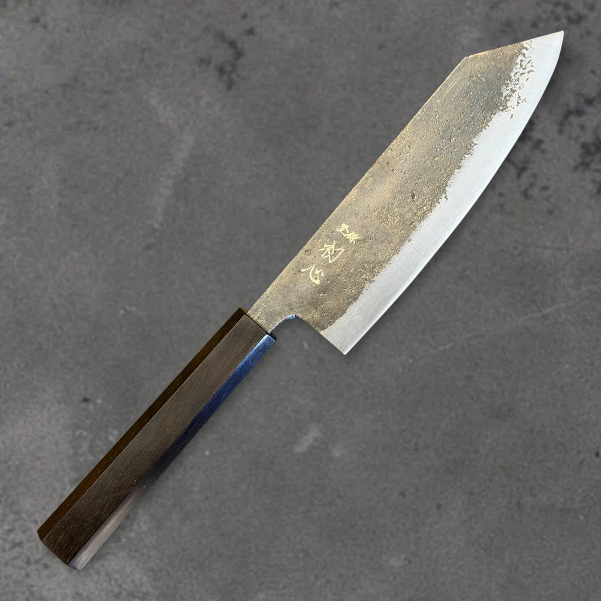 Angled front view of the Hatsukokoro Kurogane Blue #2 Kurouchi 165mm bunka with ebony handle, showing the blade shape, finish, and handle.