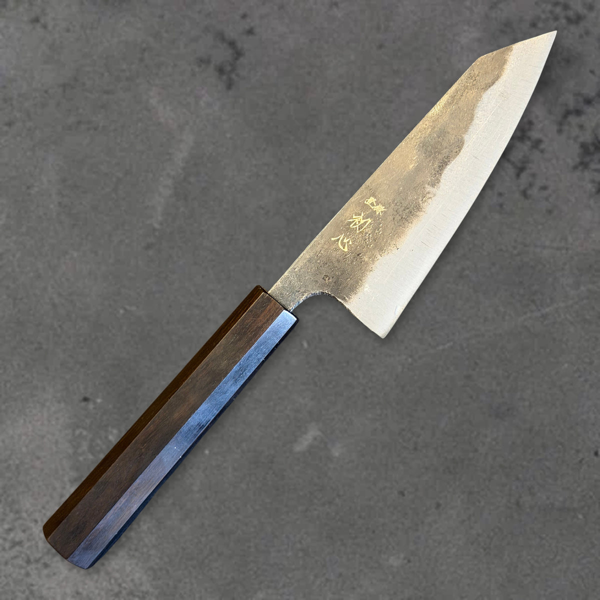 Angled front view of the Hatsukokoro Kurogane Blue #2 Kurouchi 120mm ko-bunka with ebony handle, showing the blade shape, finish, and handle.