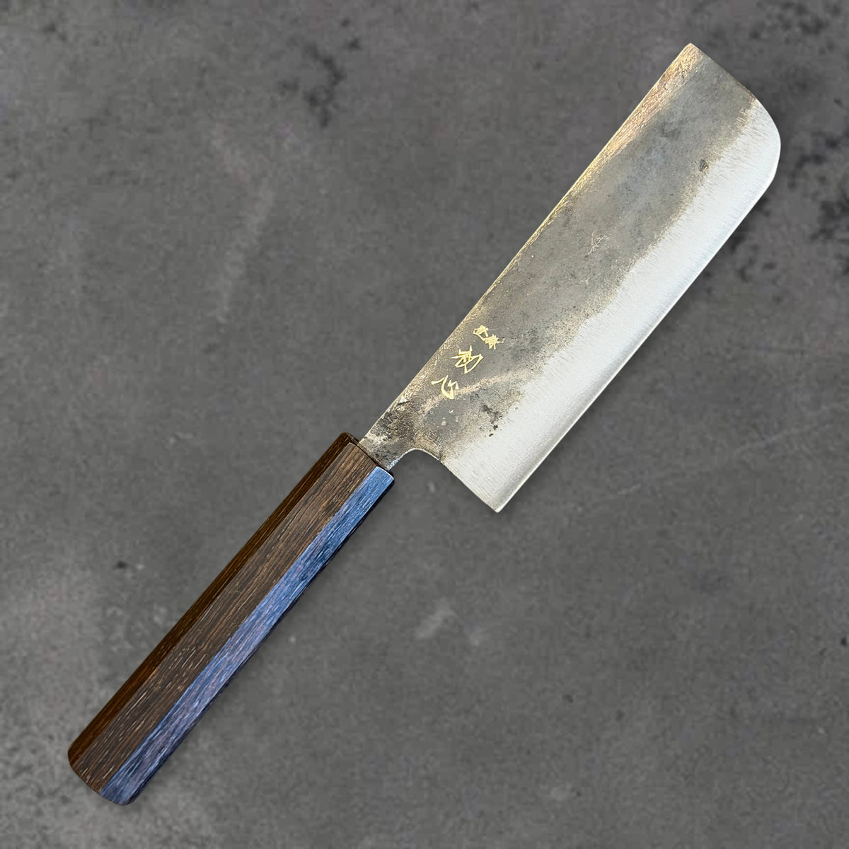 Angled front view of the Hatsukokoro Kurogane Blue #2 Kurouchi 120mm nakiri with ebony handle, showing the blade shape, finish, and handle. #Handle_Mono Ebony