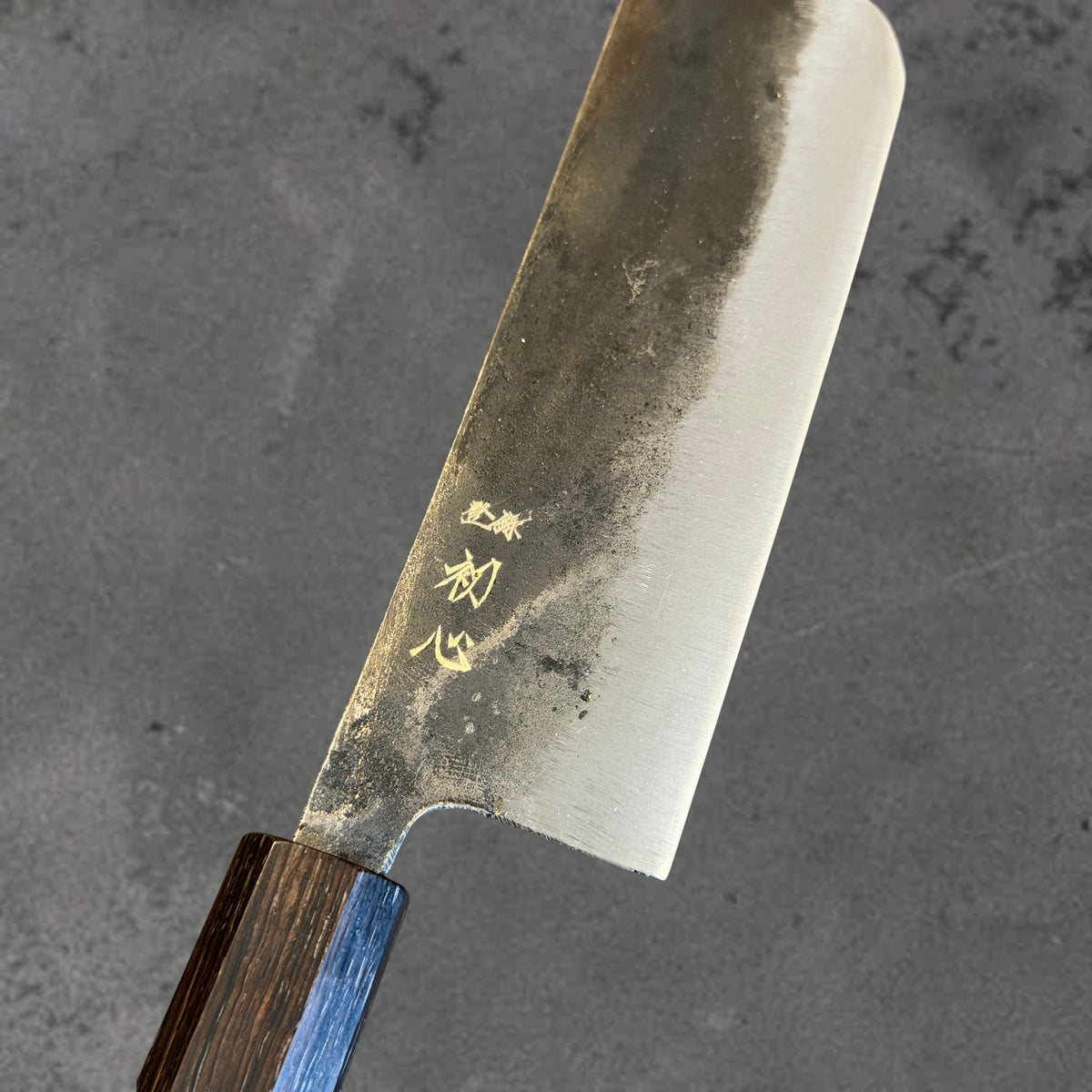 Close-up of the Kurouchi finish, blade markings, and polished bevel on the Hatsukokoro Kurogane Blue #2 Kurouchi 120mm nakiri with ebony handle. #Handle_Mono Ebony