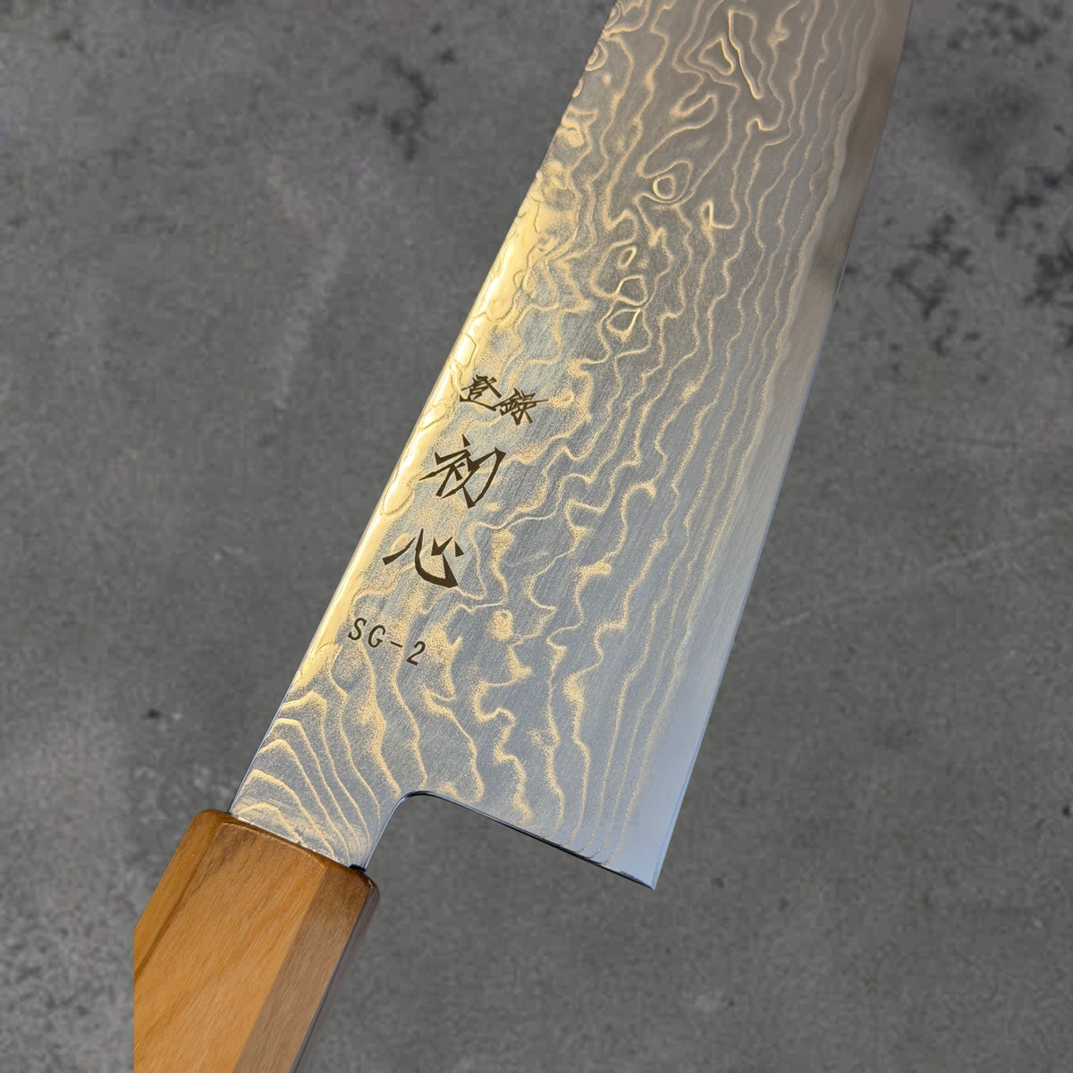 Close-up of the Damascus pattern and blade markings on the Hatsukokoro Ryuhyo SG2 Damascus 180mm bunka with olive wood handle. #Handle_Mono Olive Wood
