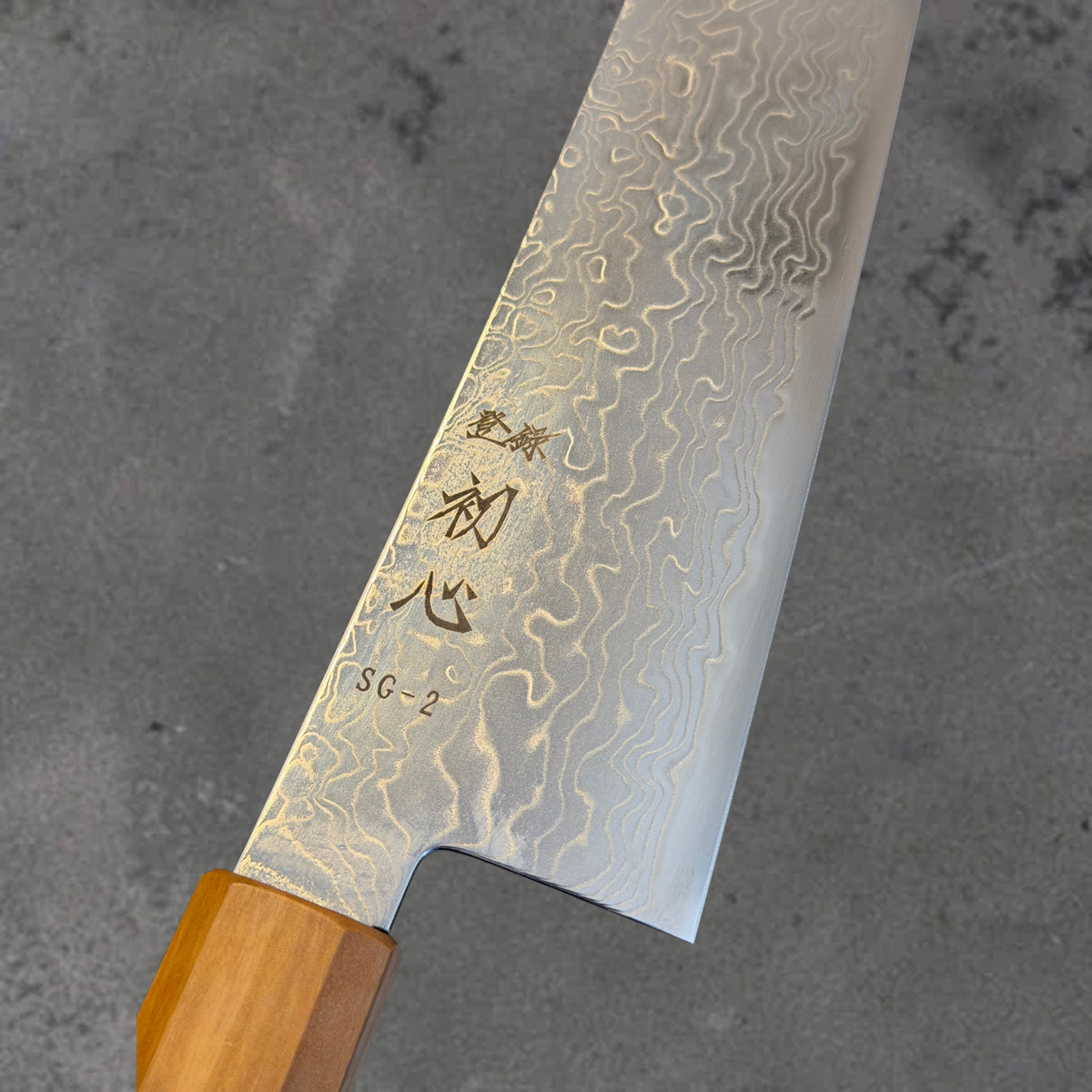Close-up of the Damascus pattern and blade markings on the Hatsukokoro Ryuhyo SG2 Damascus 210mm kiritsuke with olive wood handle.