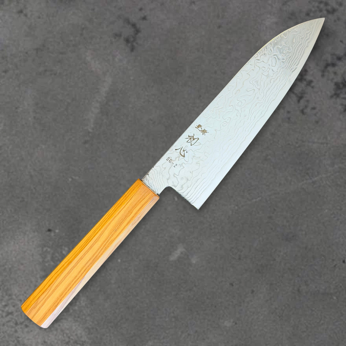 Angled front view of the Hatsukokoro Ryuhyo SG2 Damascus santoku with olive wood handle, showing the blade shape, finish, and handle.