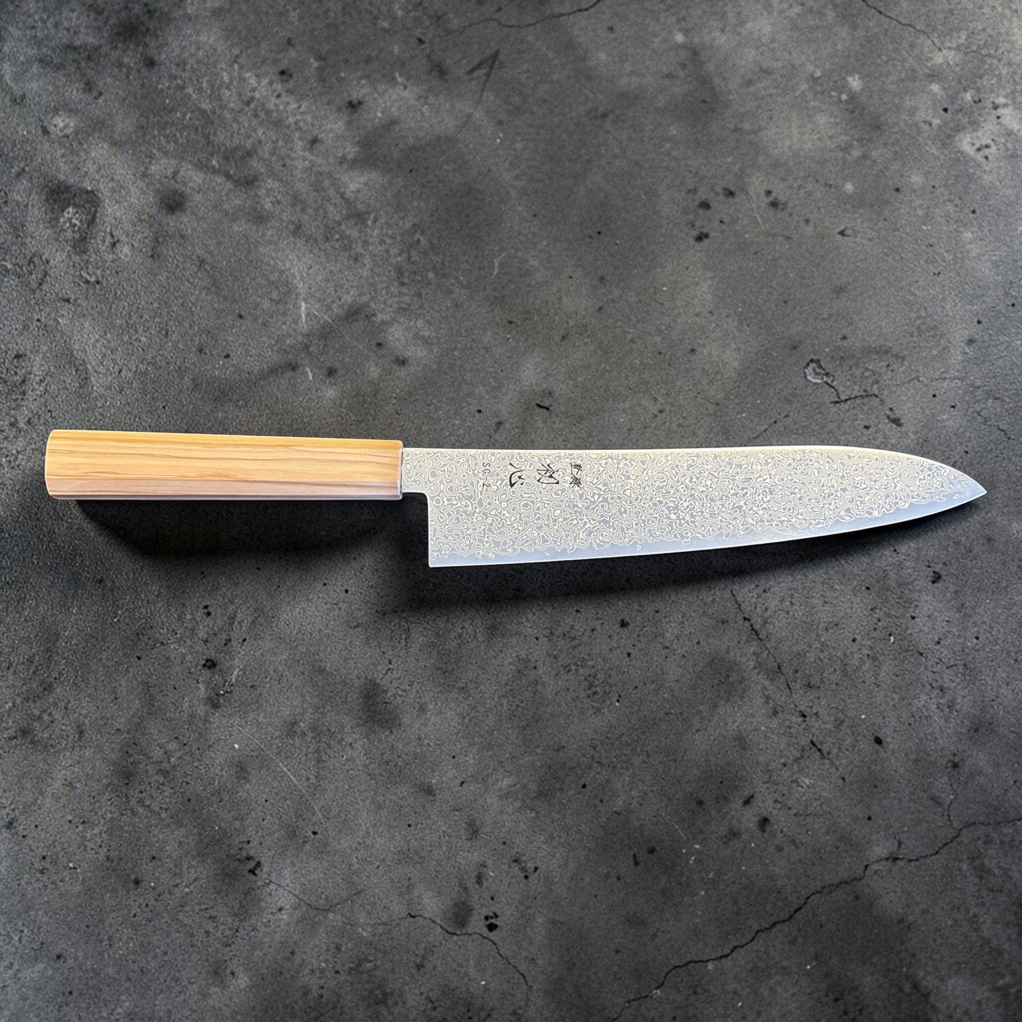 Hatsukokoro Saihyo SG2 Damascus Gyuto 210 mm with mono olive handle, side profile view showing the full blade, machi area, and etched Damascus finish.