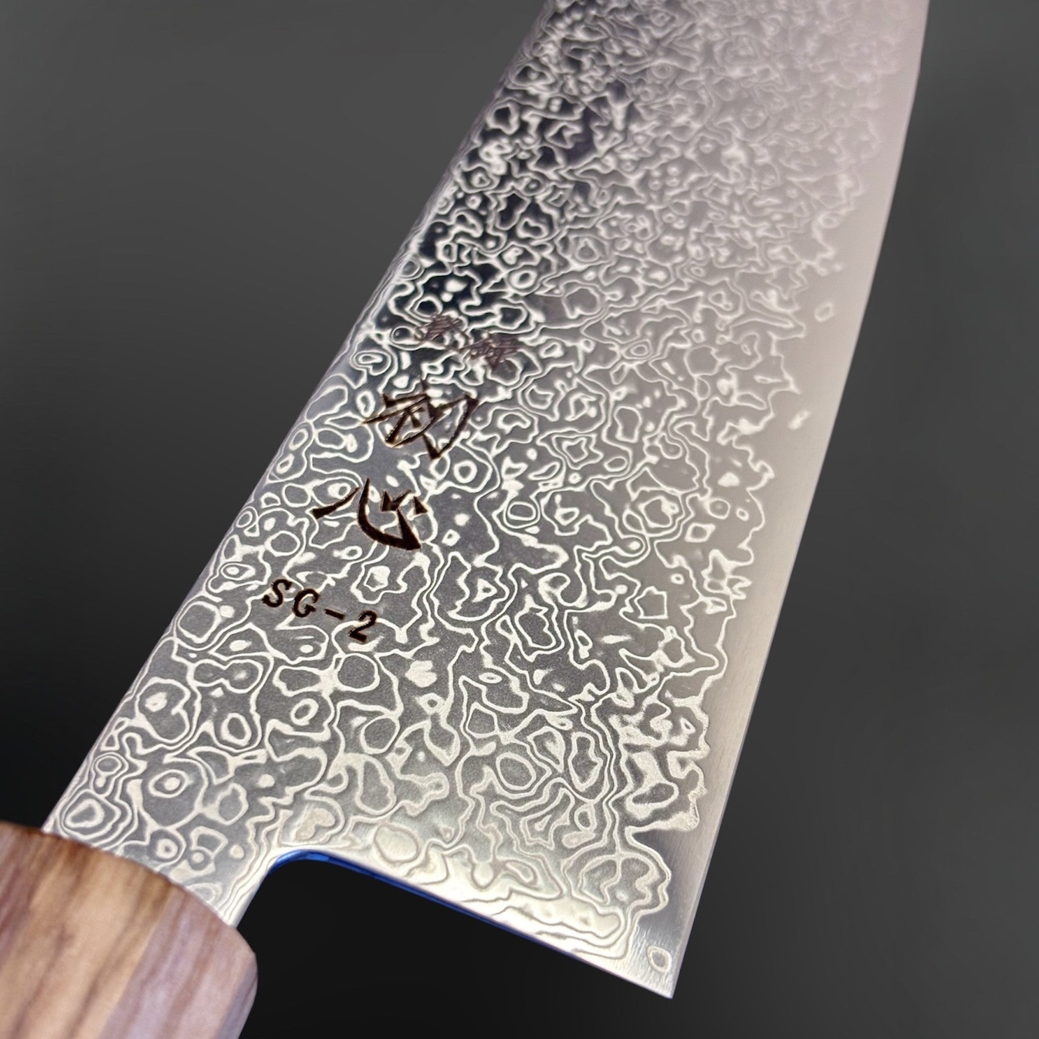 Hatsukokoro Saihyo SG2 Damascus Kiritsuke 240mm with Mono Olive Wood Handle, close-up of the SG2 Damascus blade face showing etched patterning and kanji detail near the heel.