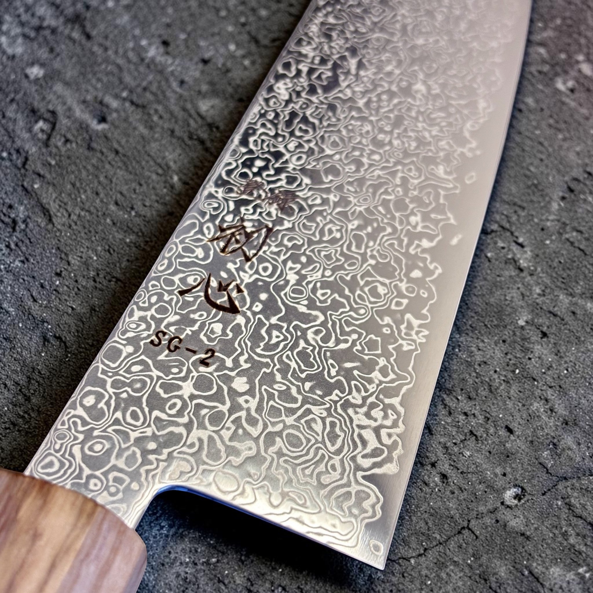 Hatsukokoro Saihyo SG2 Damascus Kiritsuke 240mm with Mono Olive Wood Handle, close-up of the SG2 Damascus blade face showing etched patterning and kanji detail near the heel.