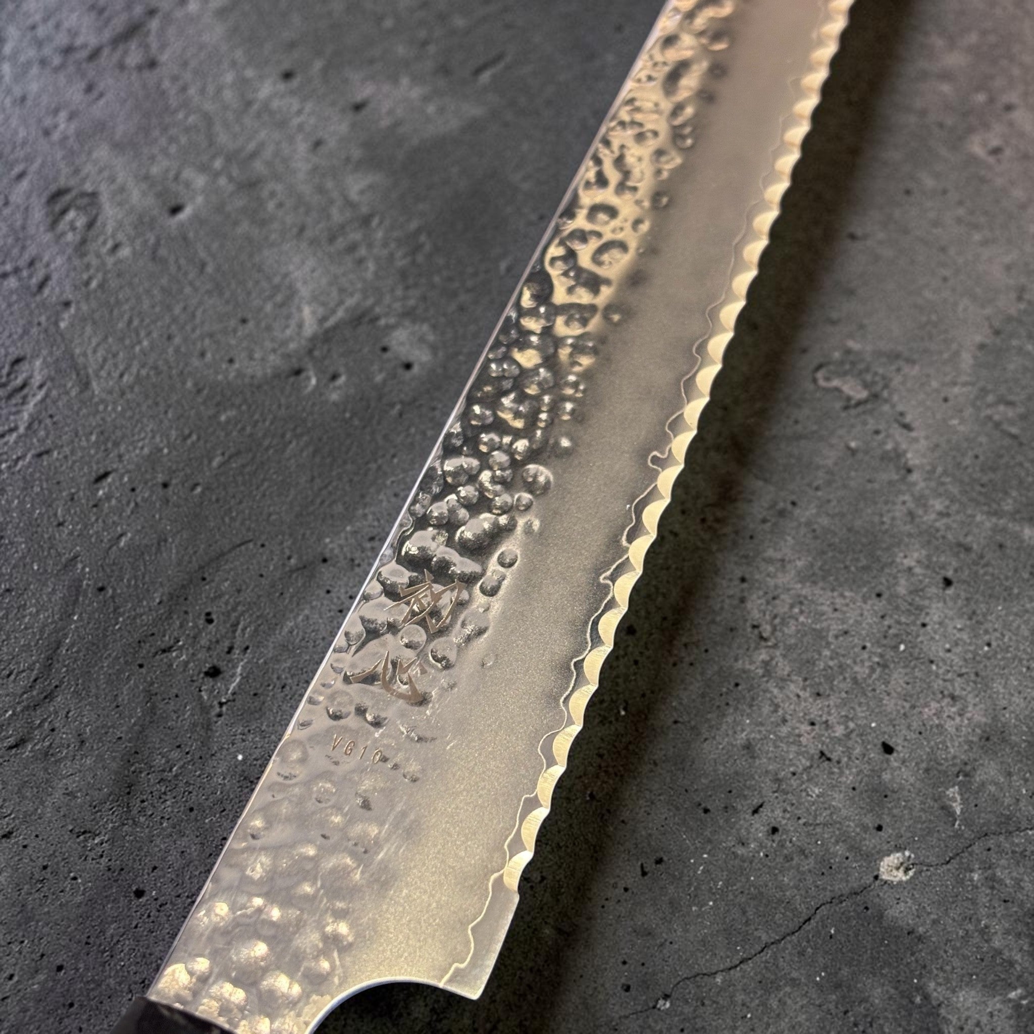 Hatsukokoro VG-10 Tsuchime Serrated Bread Knife 230 mm with burnt wood and black buffalo horn handle, close-up of hammered tsuchime blade face and serrated edge.