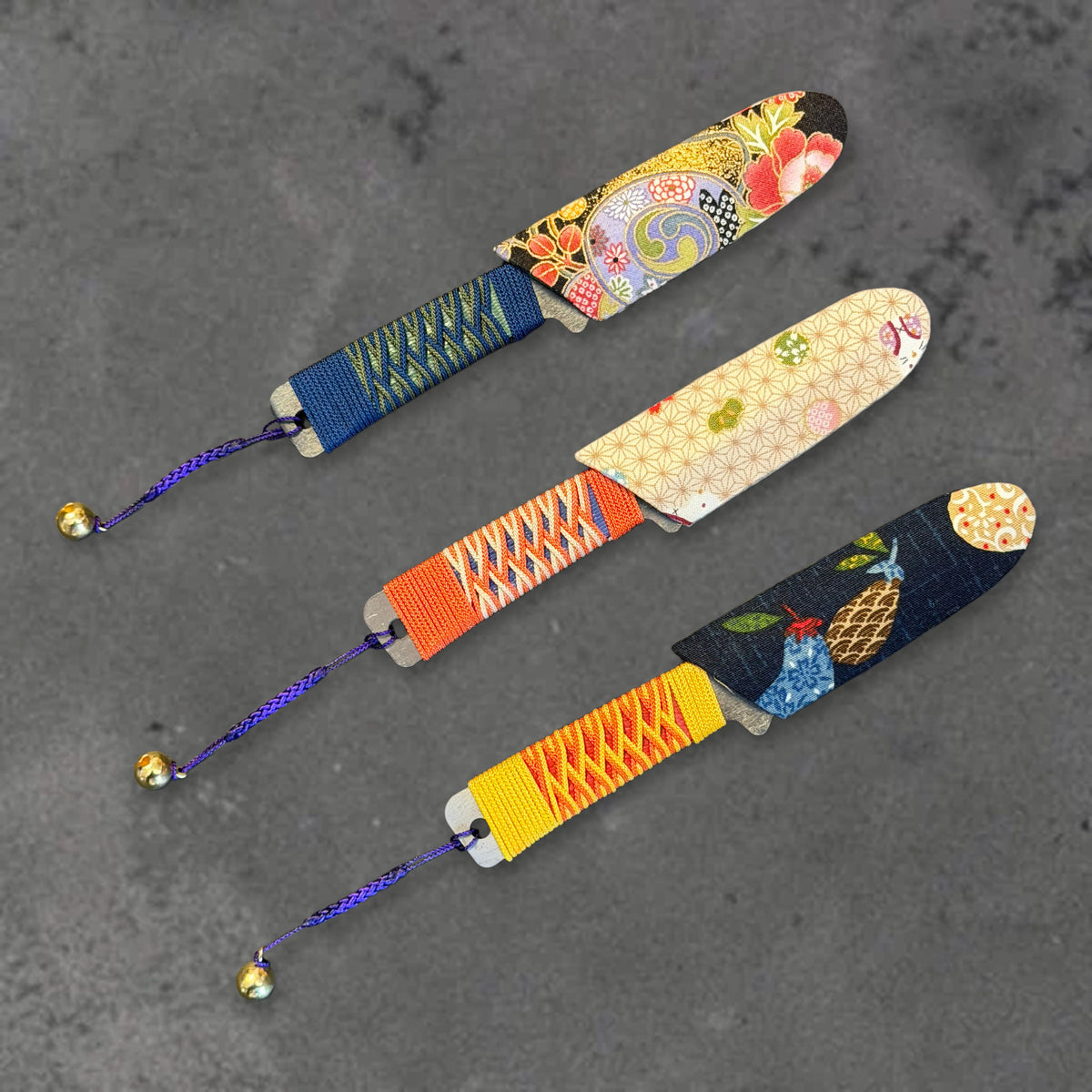 Three Higonokami Bannou knives with blue, orange, and yellow wrapped handles and patterned sheaths, arranged side by side.