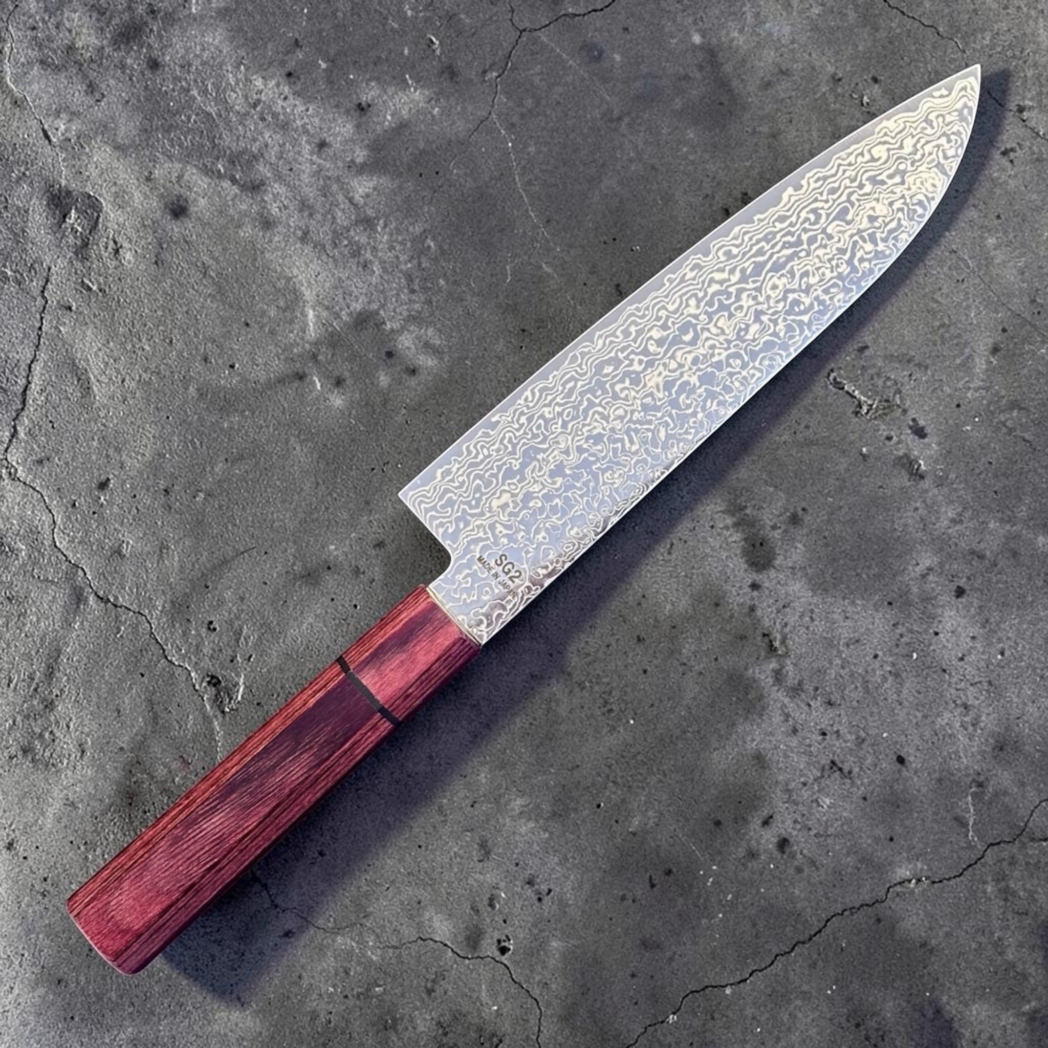 Higuchi SG2 Damascus Santoku 180 mm with red pakkawood handle, full knife angled view showing the Damascus blade pattern.