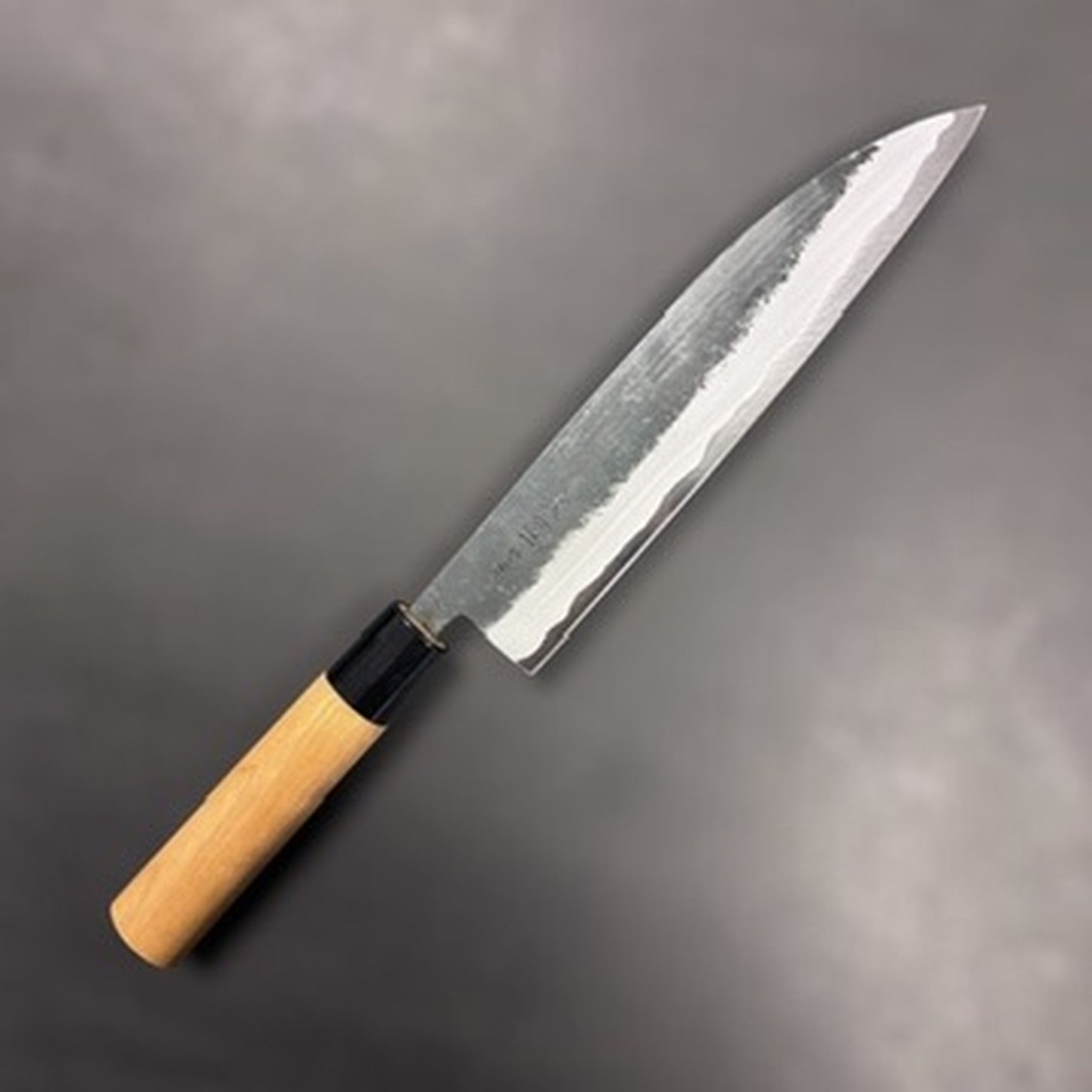 Hinokuni Aogami Super Kurouchi Gyuto 210 mm, three‑quarter view showing the kurouchi finish and light wa‑handle with black ferrule.