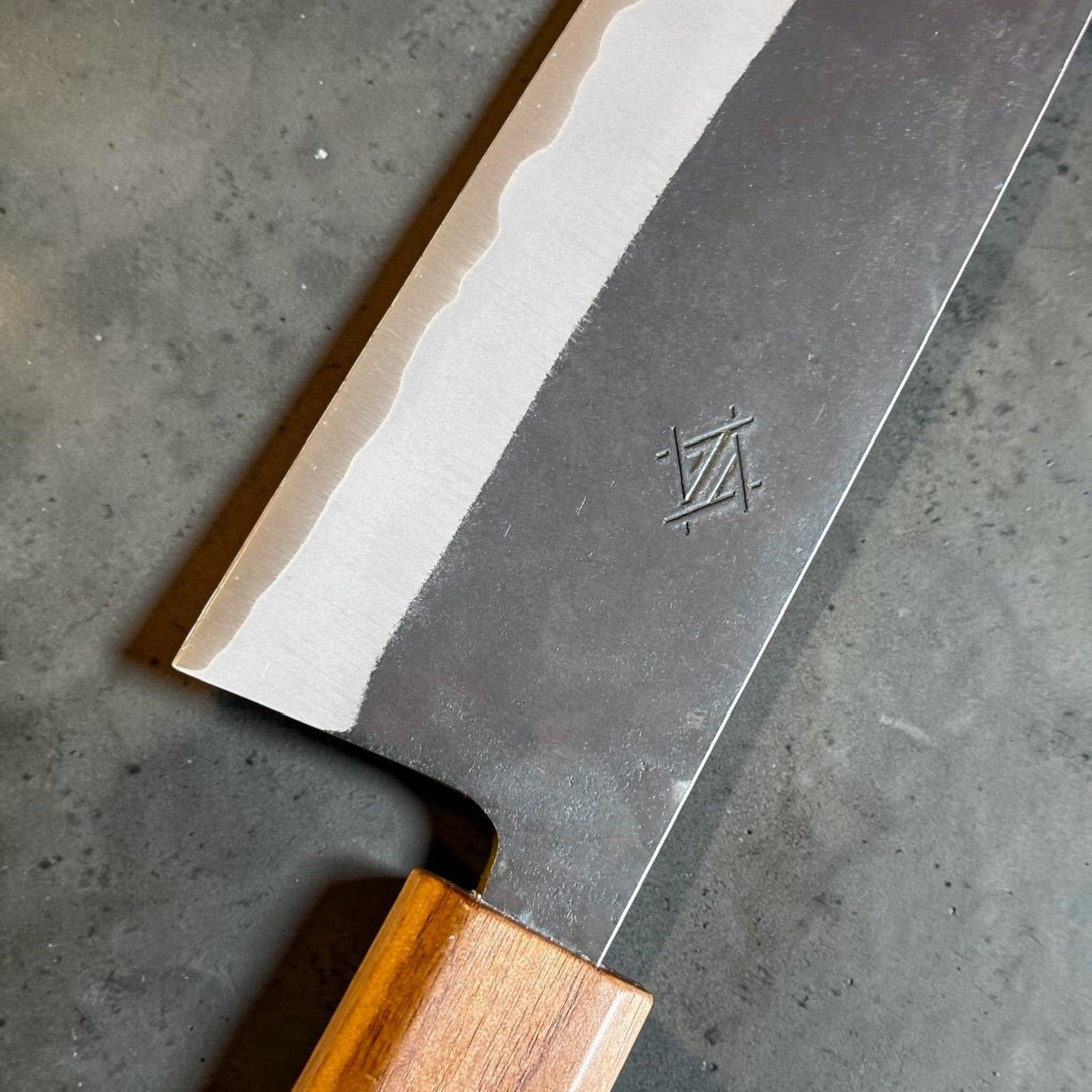 Imai Stainless Clad Aogami Super Kurouchi Bunka 183 mm with Sanjo walnut and maple stripe handle, close-up of the kurouchi finish and polished bevel.