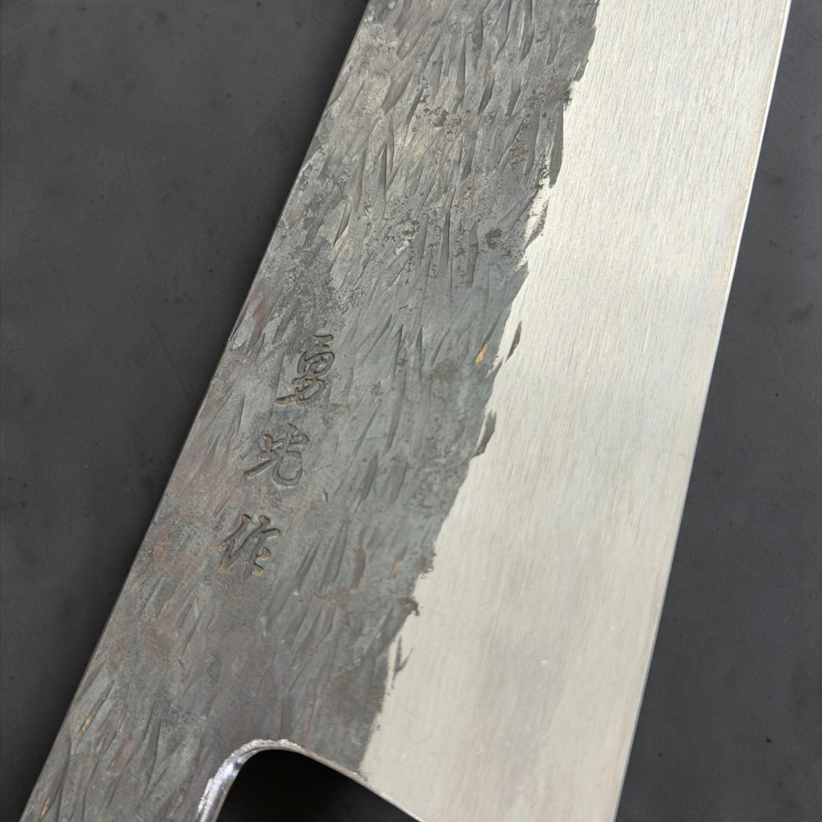 Close-up of Isamitsu maker engraving, kurouchi tsuchime texture and polished bevel