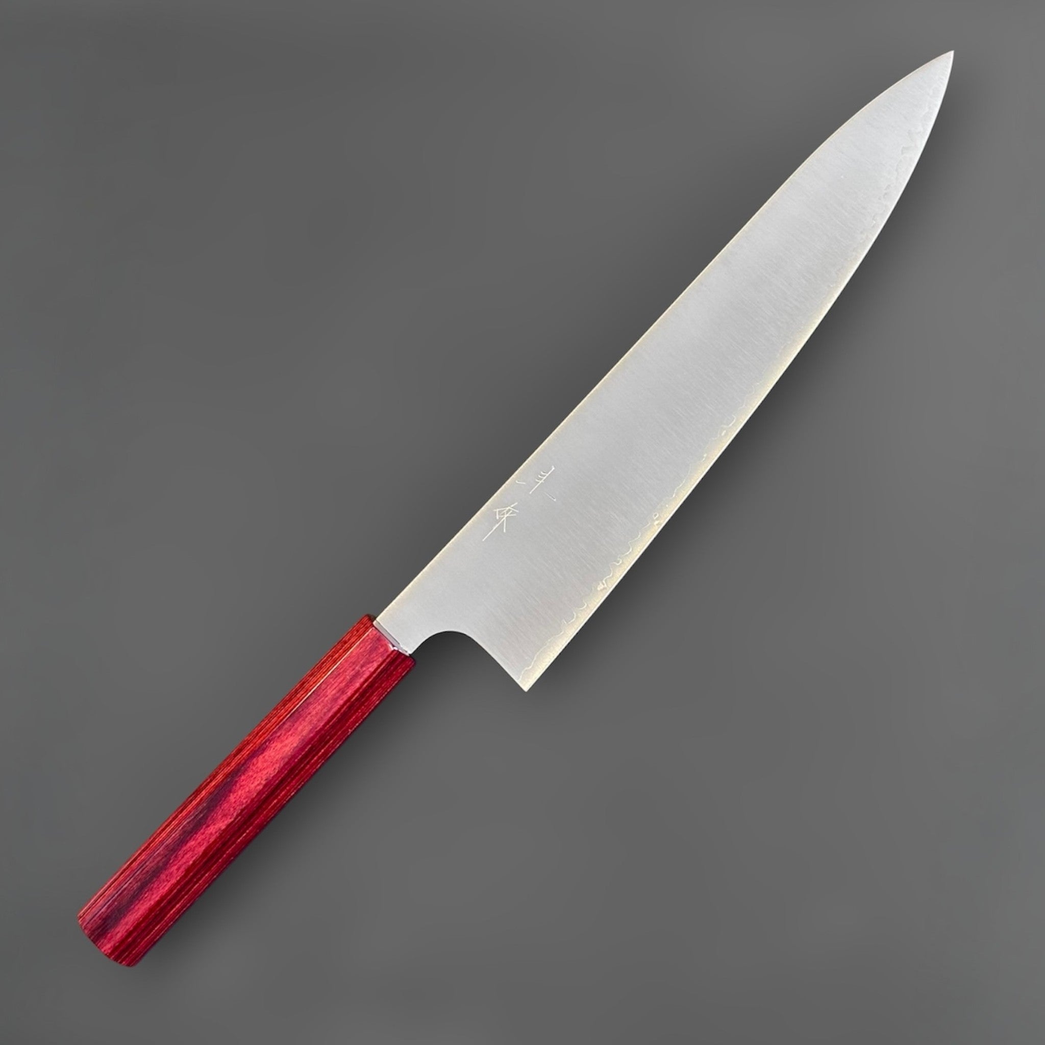 shi SG2 Gyuto 240 mm with red lacquer handle, angled front-side close-up highlighting the engraved kanji, polished satin blade, and fine tip geometry.