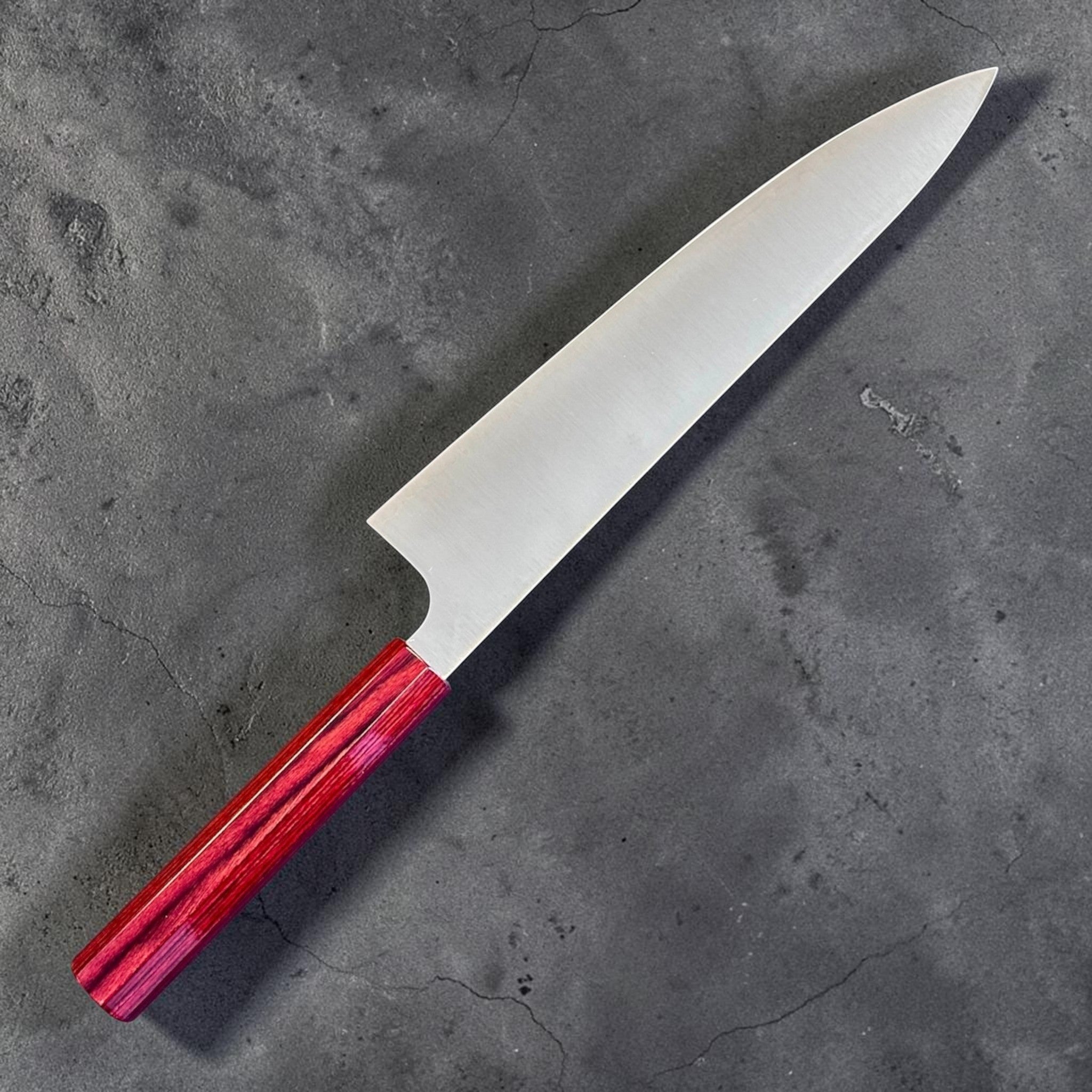 shi SG2 Gyuto 240 mm with red lacquer handle, angled reverse-side view emphasizing the extra-long gyuto profile, thin grind, and distal taper.