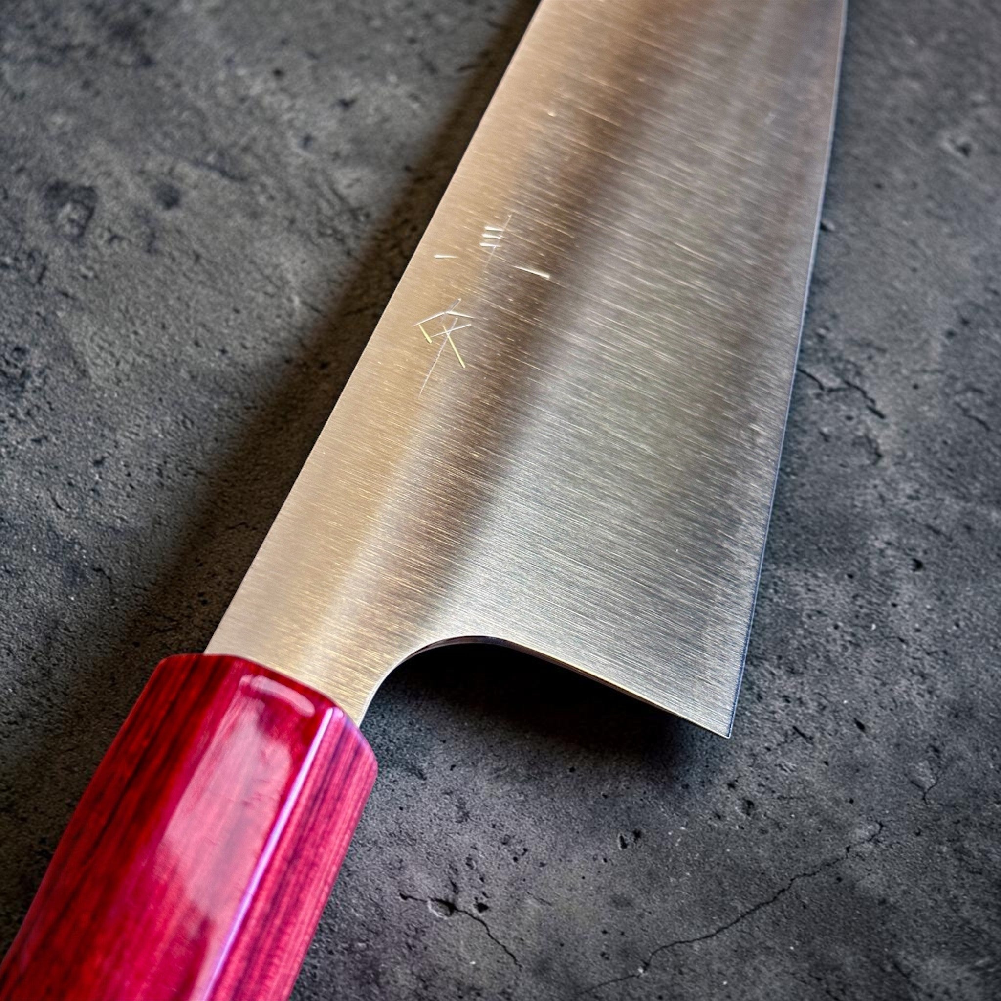 shi SG2 Gyuto 240 mm with red lacquer handle, spine view close-up showing the extremely thin grind and precise taper toward the tip.