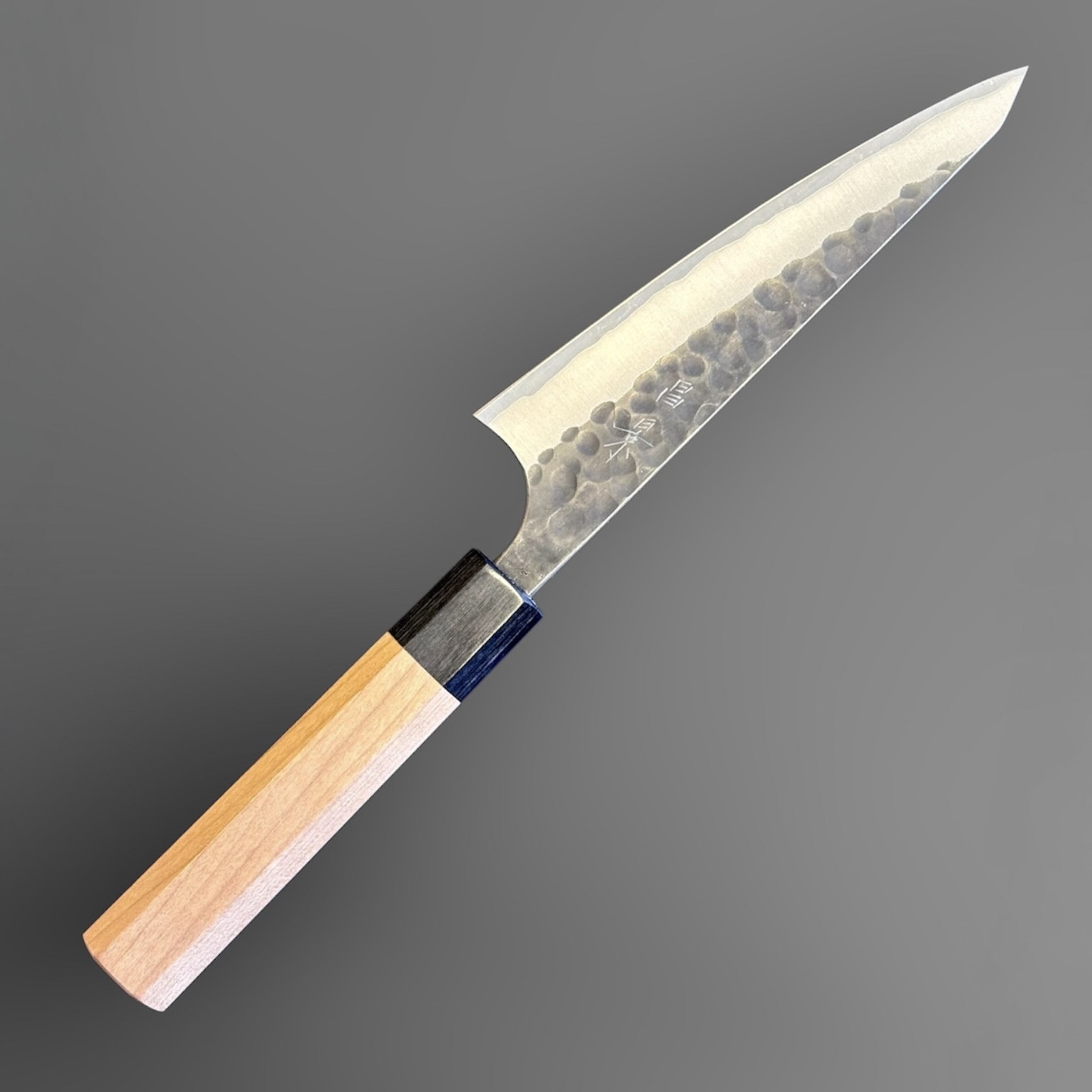 Masakage Koishi Honesuki Japanese knife, angled front product view showing hammered kurouchi-style blade finish and light wood wa handle.