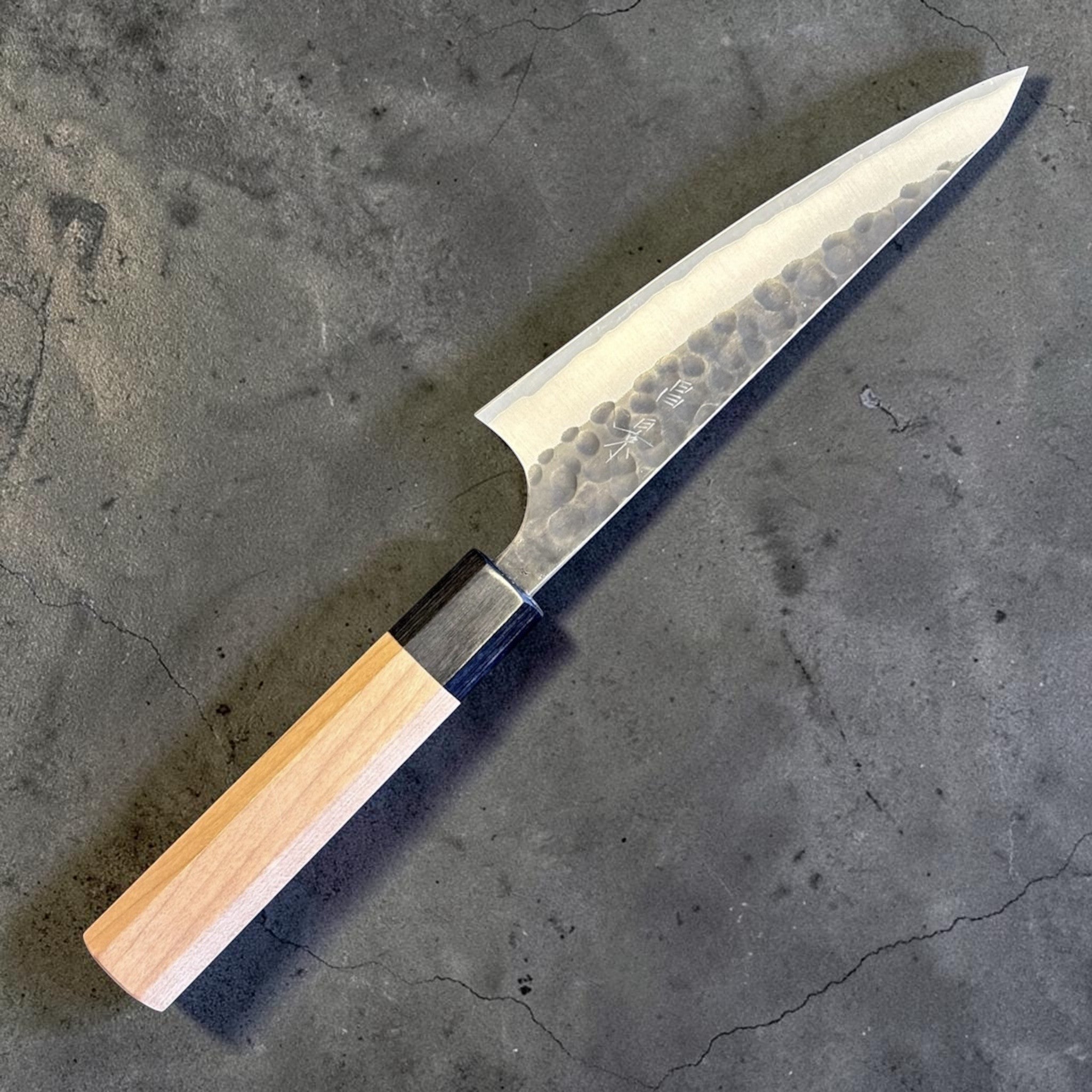 Masakage Koishi Honesuki Japanese knife, angled front product view showing hammered kurouchi-style blade finish and light wood wa handle.
