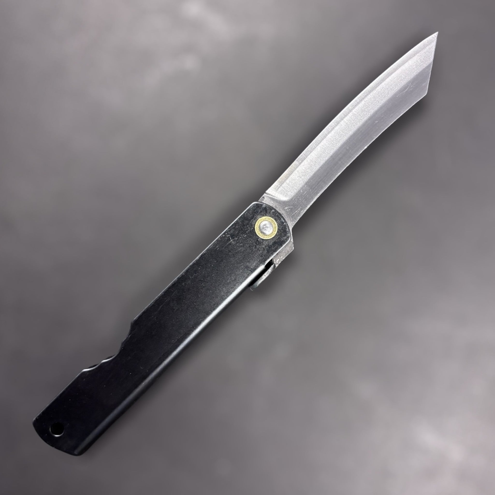 Reverse side of Nagao Higonokami SK carbon steel medium friction folder with plain black handle and SK carbon blade, studio-lit on dark background.