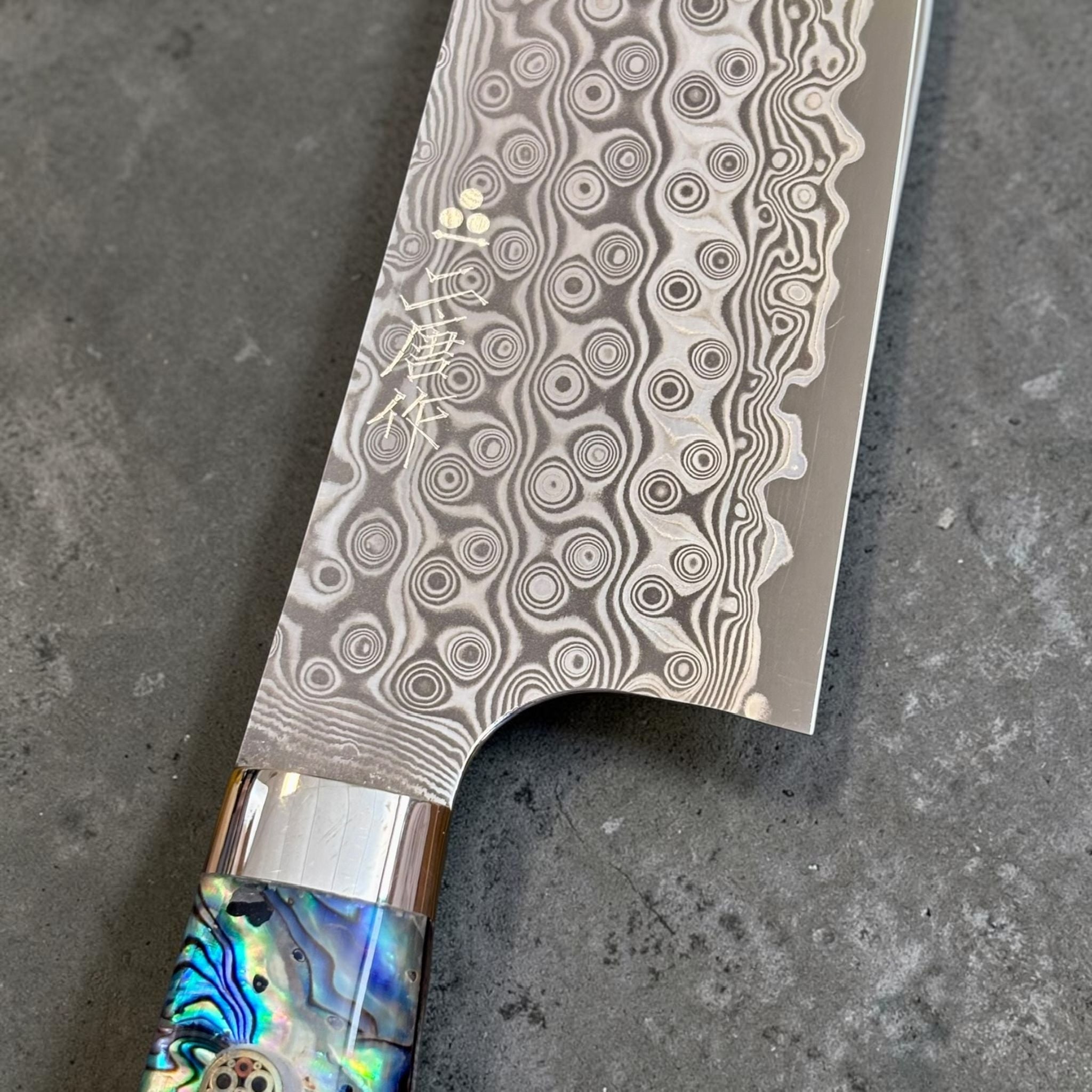 Nigara Anmon Damascus Santoku SG2 180 mm with Abalone Western Handle, close-up of Anmon Damascus pattern and maker's kanji near the heel.