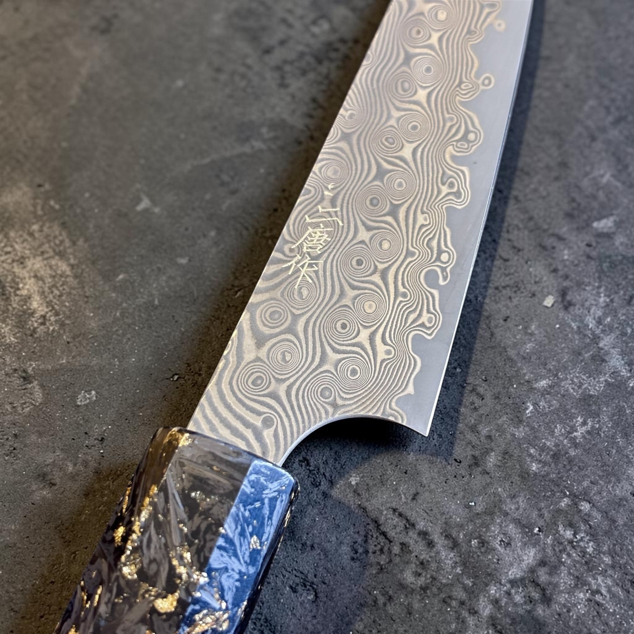 Nigara Anmon SG2 Petty 120 mm with carbon fiber and gold fleck handle, close-up of Anmon damascus pattern near the heel.