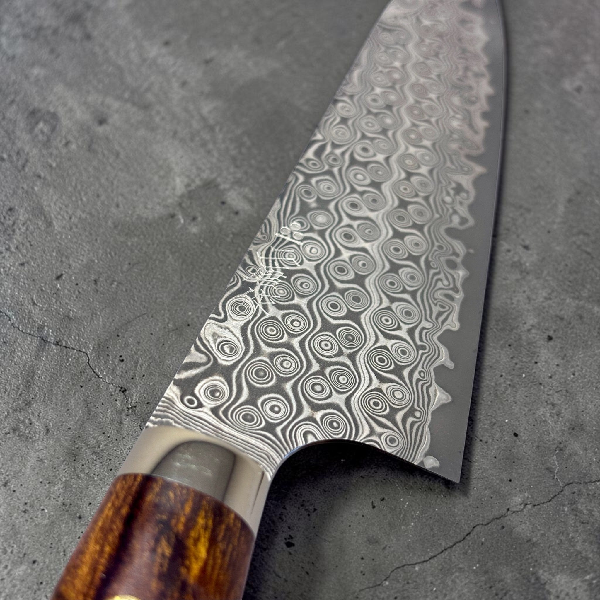 Nigara Hamono Anmon SG2 210 mm Gyuto with ironwood western handle, close-up of SG2 Anmon Damascus blade pattern near the heel.