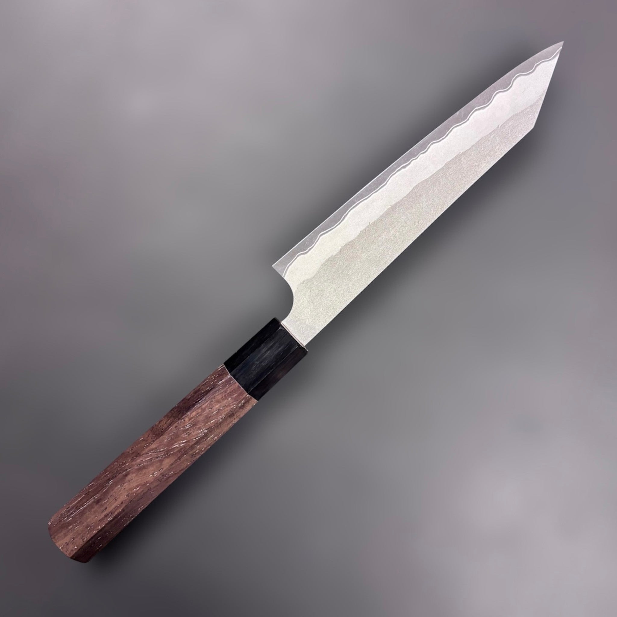 Nigara Hamono Aogami Super Tsuchime Kiritsuke Petty 150 mm with walnut handle, angled view, opposite side of blade on gray background.