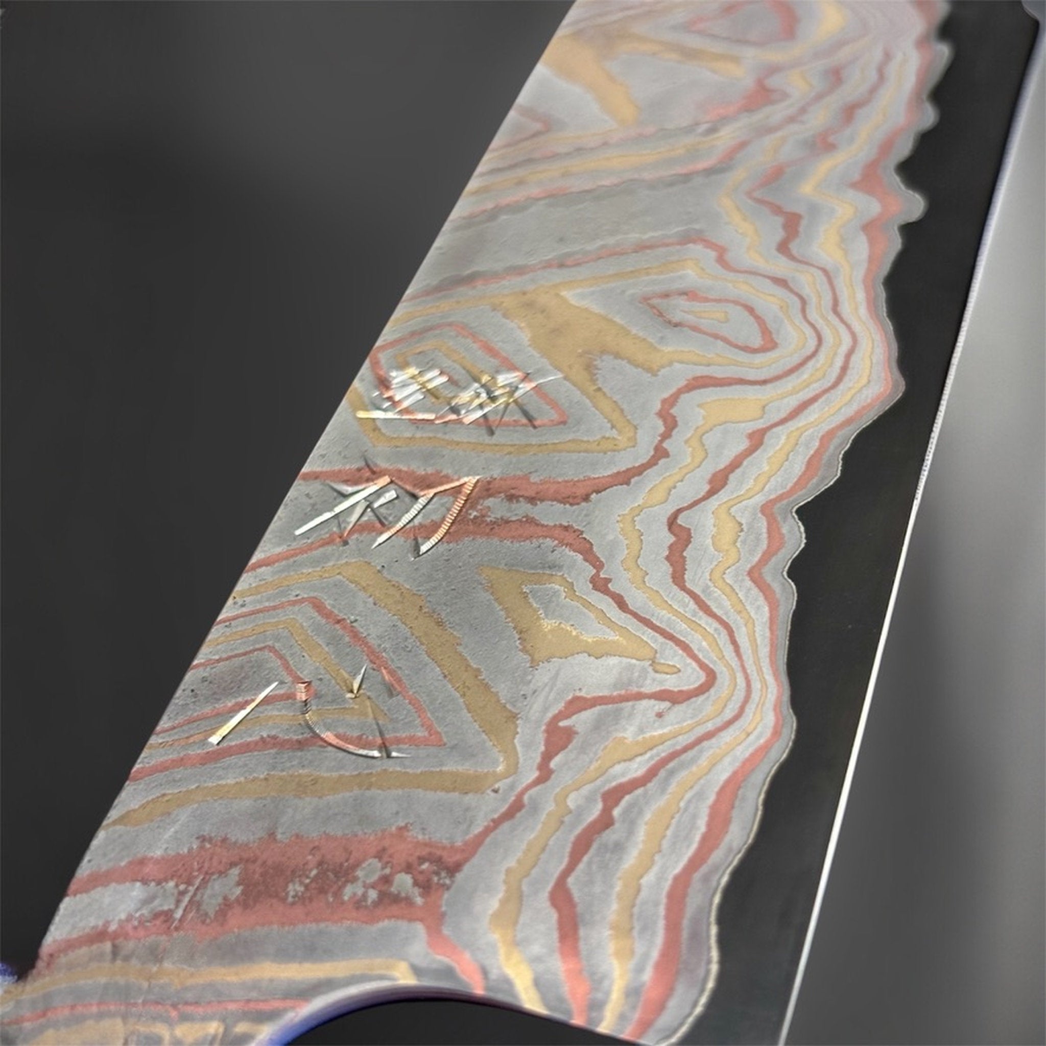 Close-up of the Nigara Irodori Blue #2 Rainbow Damascus Santoku 180 mm blade, showing the engraved kanji and intricate pink, gold, and silver damascus layers.