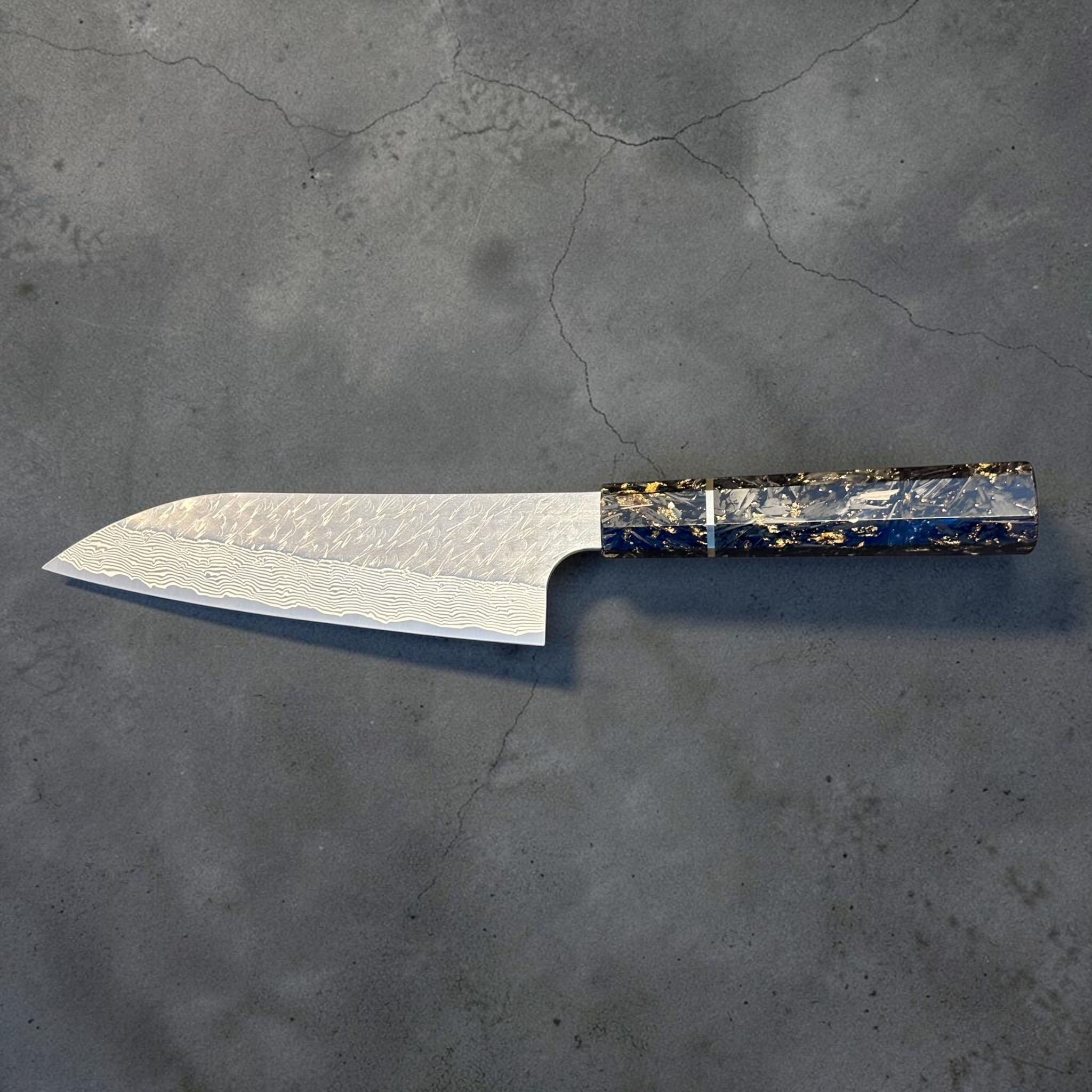 Reverse profile of the Nigara SG-STRIX Ko Santoku 150 mm featuring a custom carbon fiber and gold fleck wa handle with beautifully etched Damascus cladding.