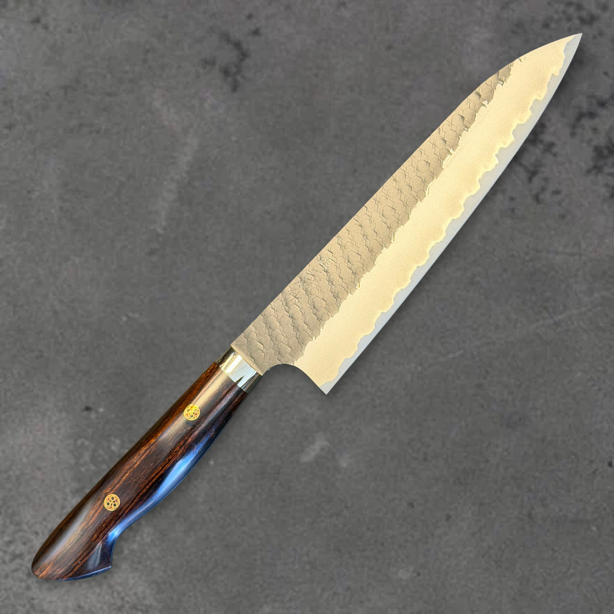 Angled front view of the Nigara SG2 Kurouchi Tsuchime 210mm gyuto with ironwood handle, showing the blade shape, finish, and handle.