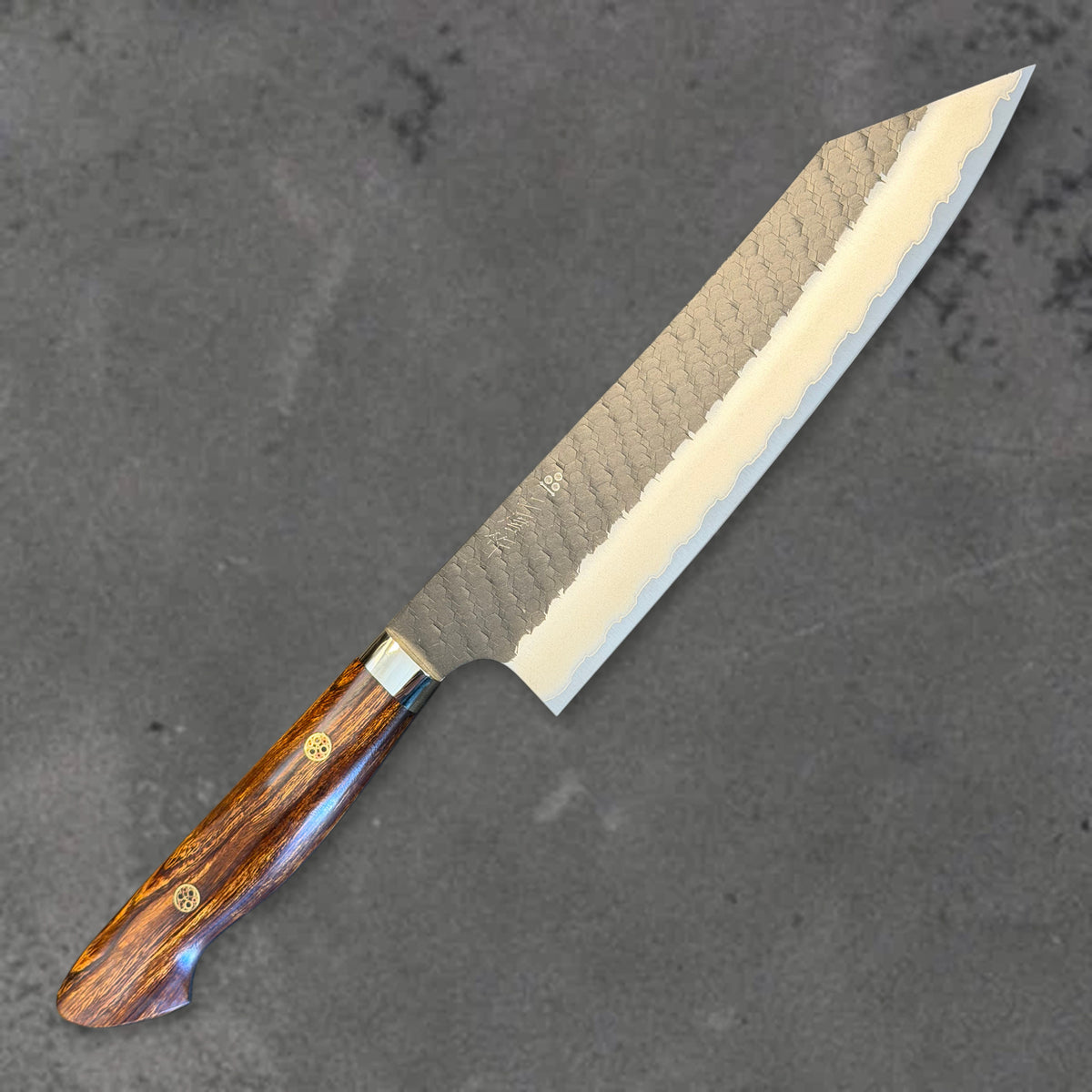 Angled front view of the Nigara SG2 Kurouchi Tsuchime 210mm kiritsuke with ironwood handle, showing the blade shape, finish, and handle.