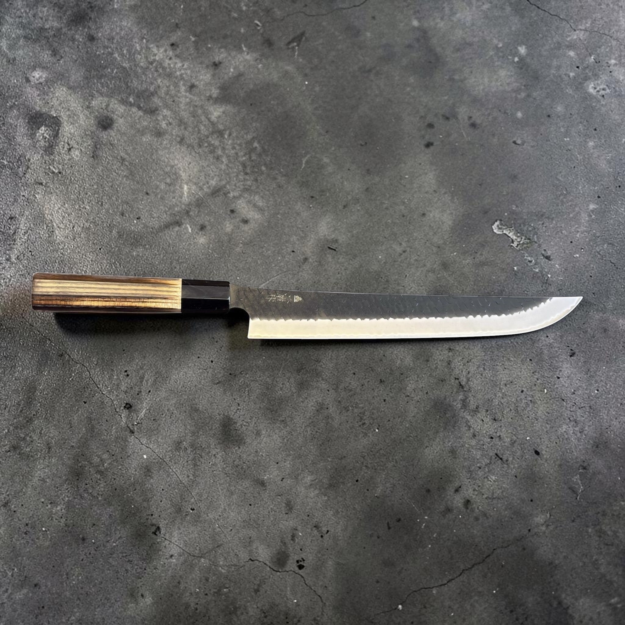 Nigara SG2 Tsuchime Kurouchi Sakimaru Sujihiki 270 mm, reverse side profile with visible kanji, hammered kurouchi texture, and polished bevel.