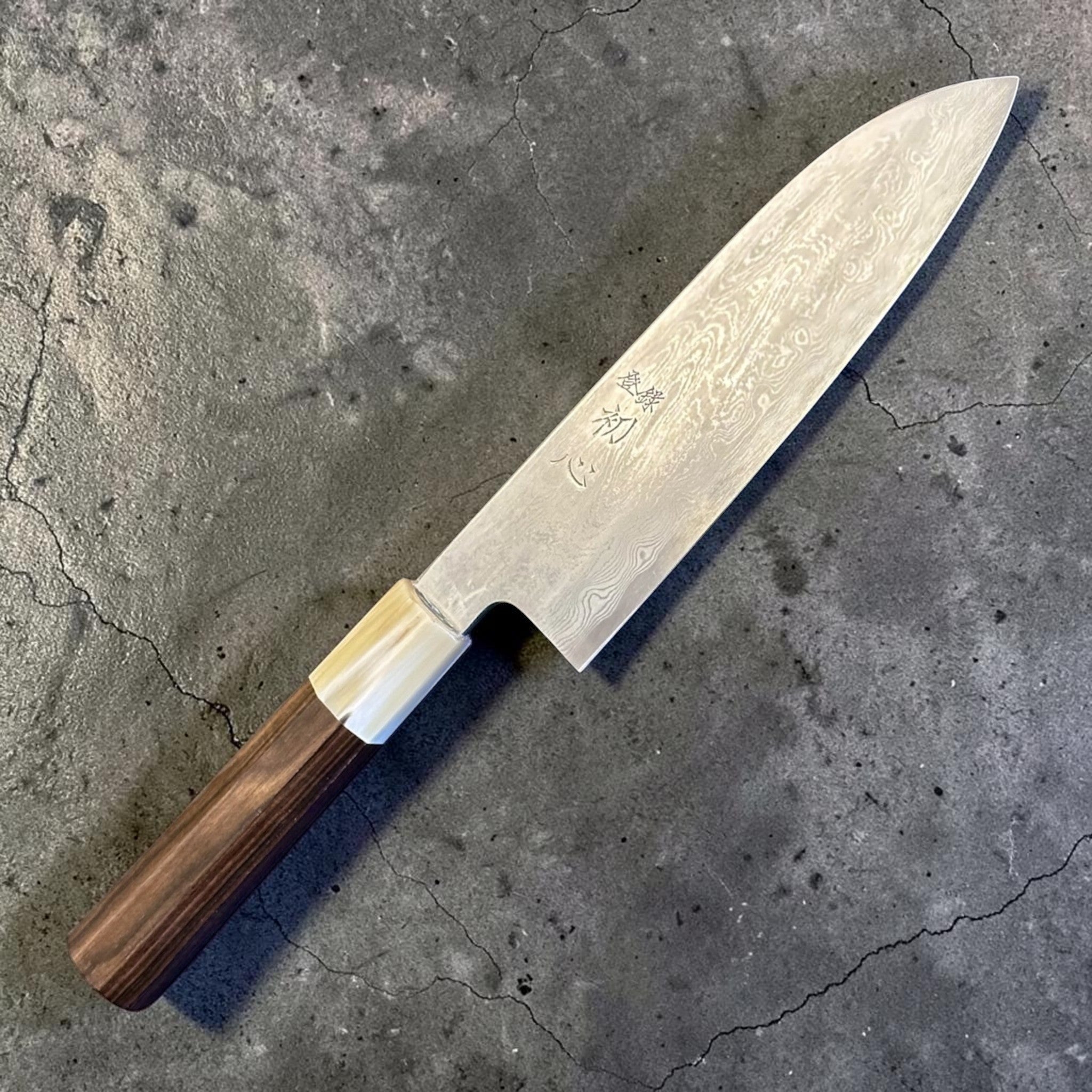 Satoshi Nakagawa Blue #1 Damascus Santoku with ebony and horn handle, angled full product view showing the flowing Damascus pattern and polished blade face.