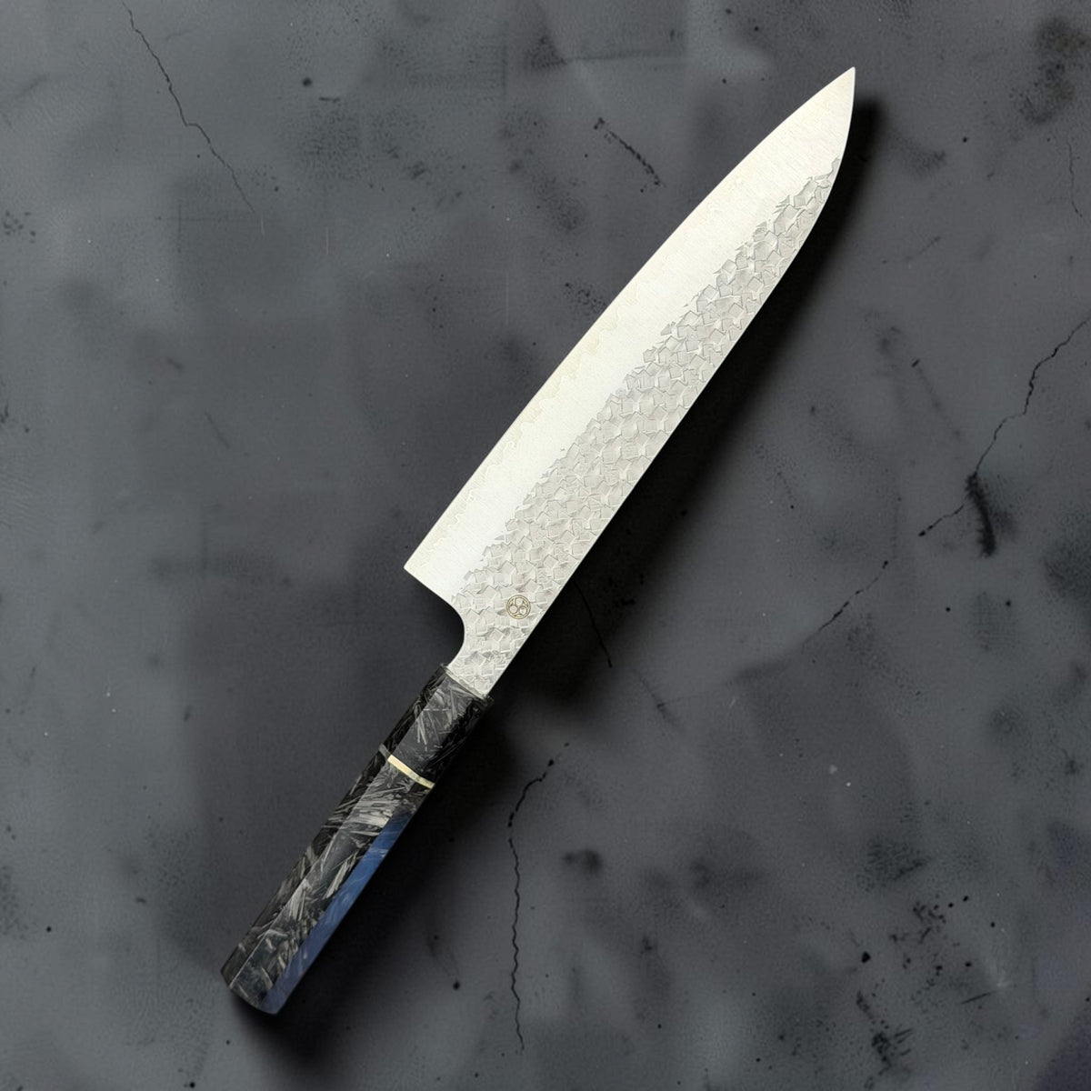 Reverse angled view of the Shibata Arare SG2 gyuto 210mm showing the geometric hammered finish and carbon fiber handle.