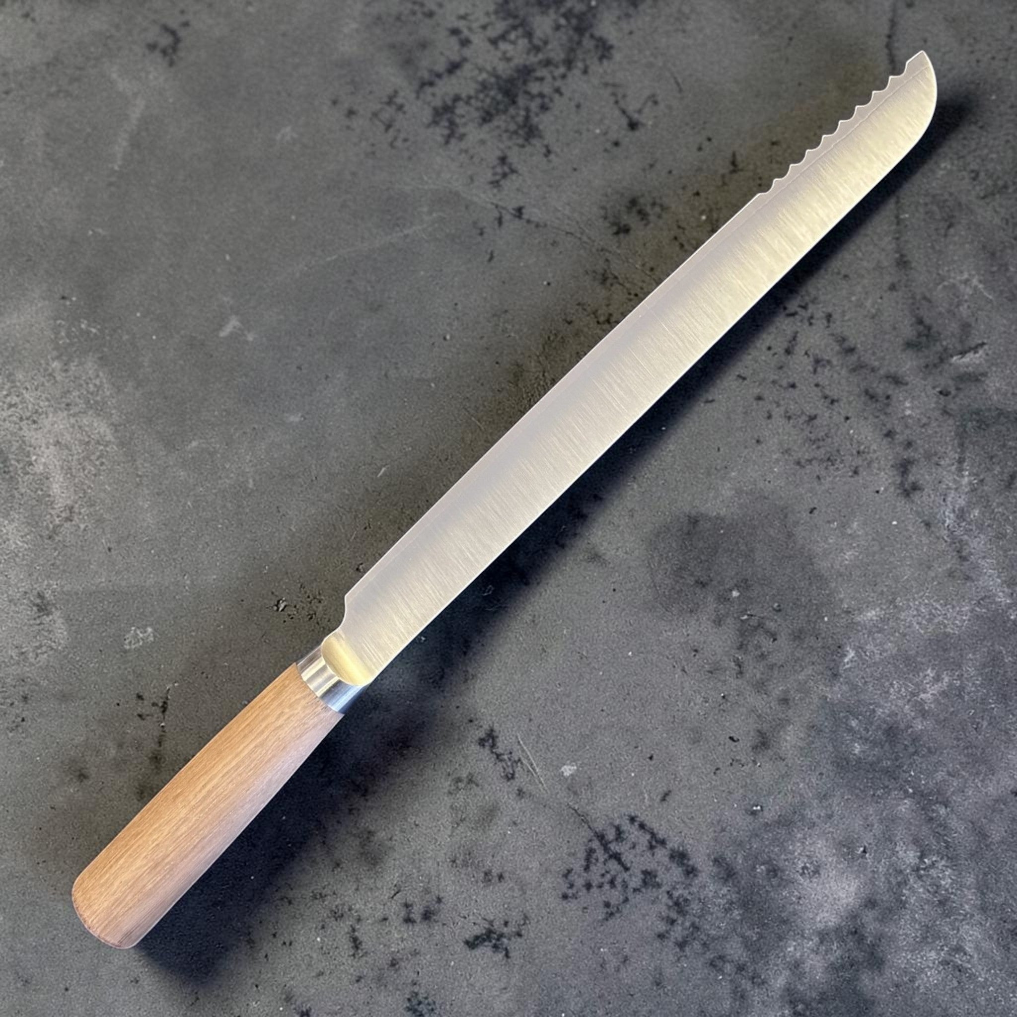 Tadafusa SLD Bread Knife with light wood handle, angled reverse view showing the long brushed blade and scalloped teeth near the tip.
